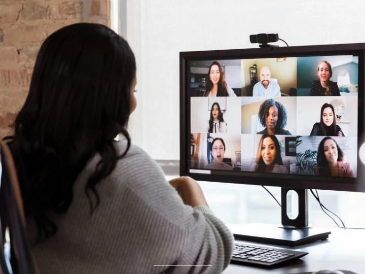Photo of Black woman and life coach facilitating a group coaching virtual session at her desk with an exposed brick wall.