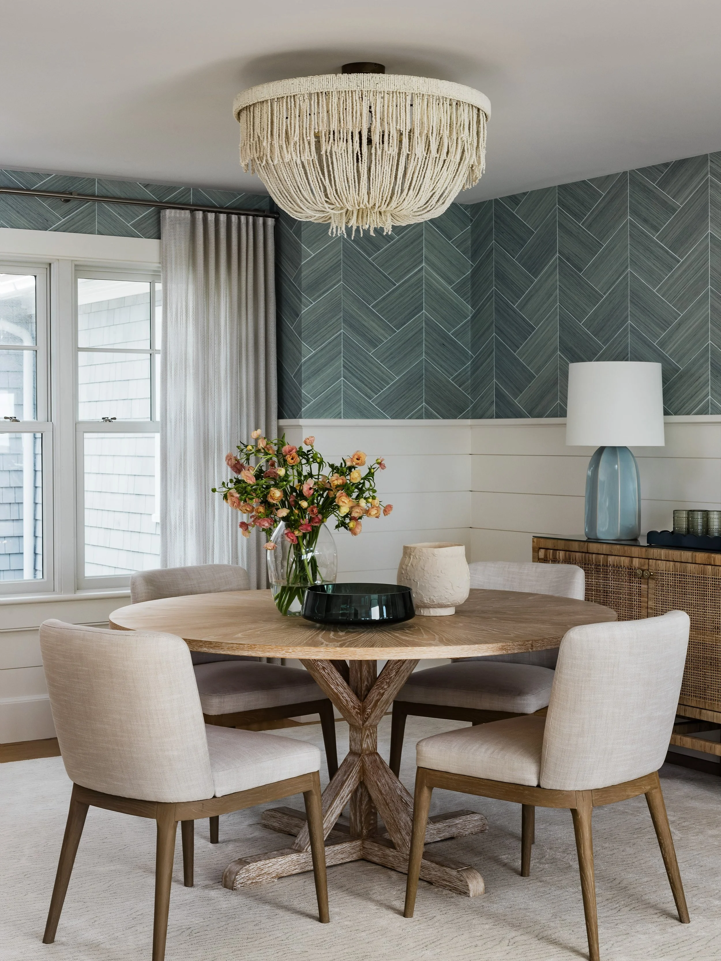This room could have leaned entirely tailored. Patterned grasscloth, clean shiplap, chairs with crisp lines, it&rsquo;s a space built on structure.

Then the chandelier. Fringe made from strands of beading, soft where everything else is precise. It&r