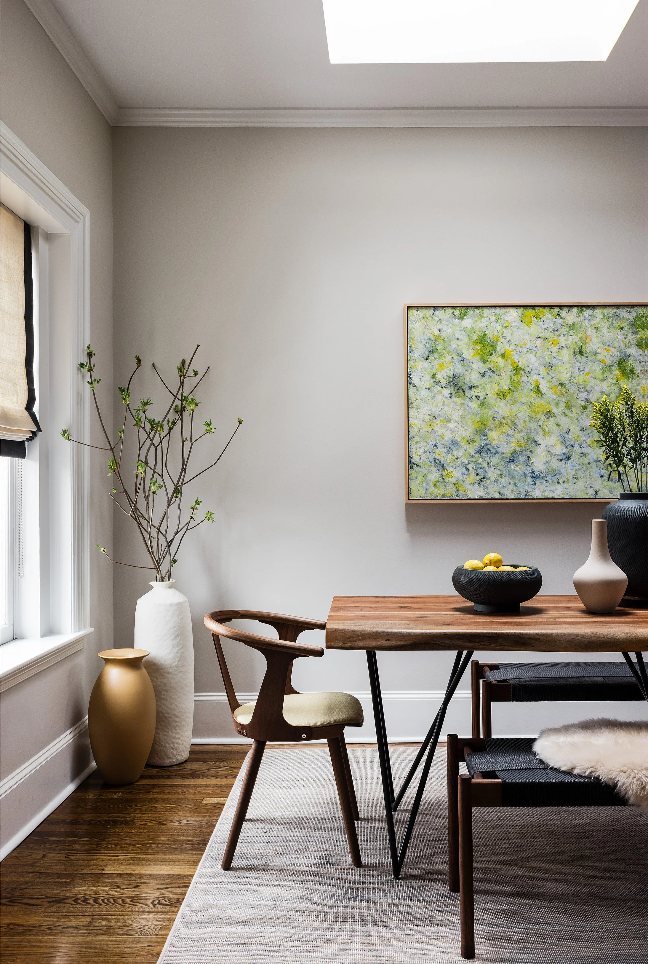 A dining room with a wooden table, modern chairs, and decorative vases, featuring a white wall and an abstract painting.