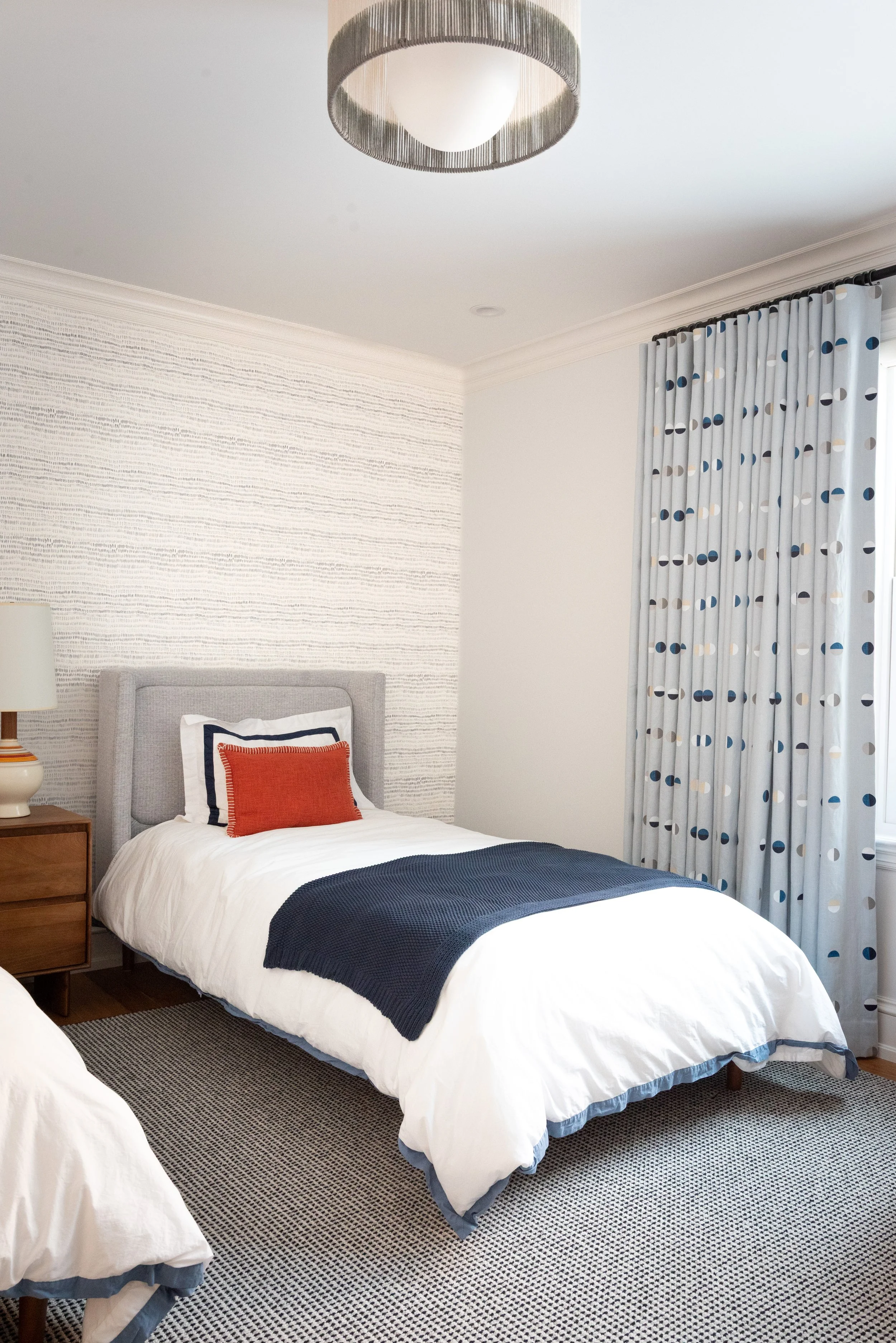 A bedroom with a bed, nightstand, table lamp, curtains, and a ceiling light fixture.