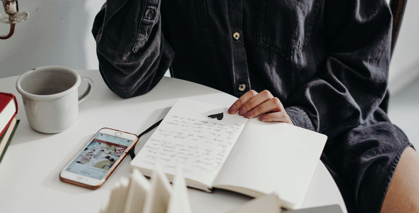 person sitting at table with phone, coffee, journal