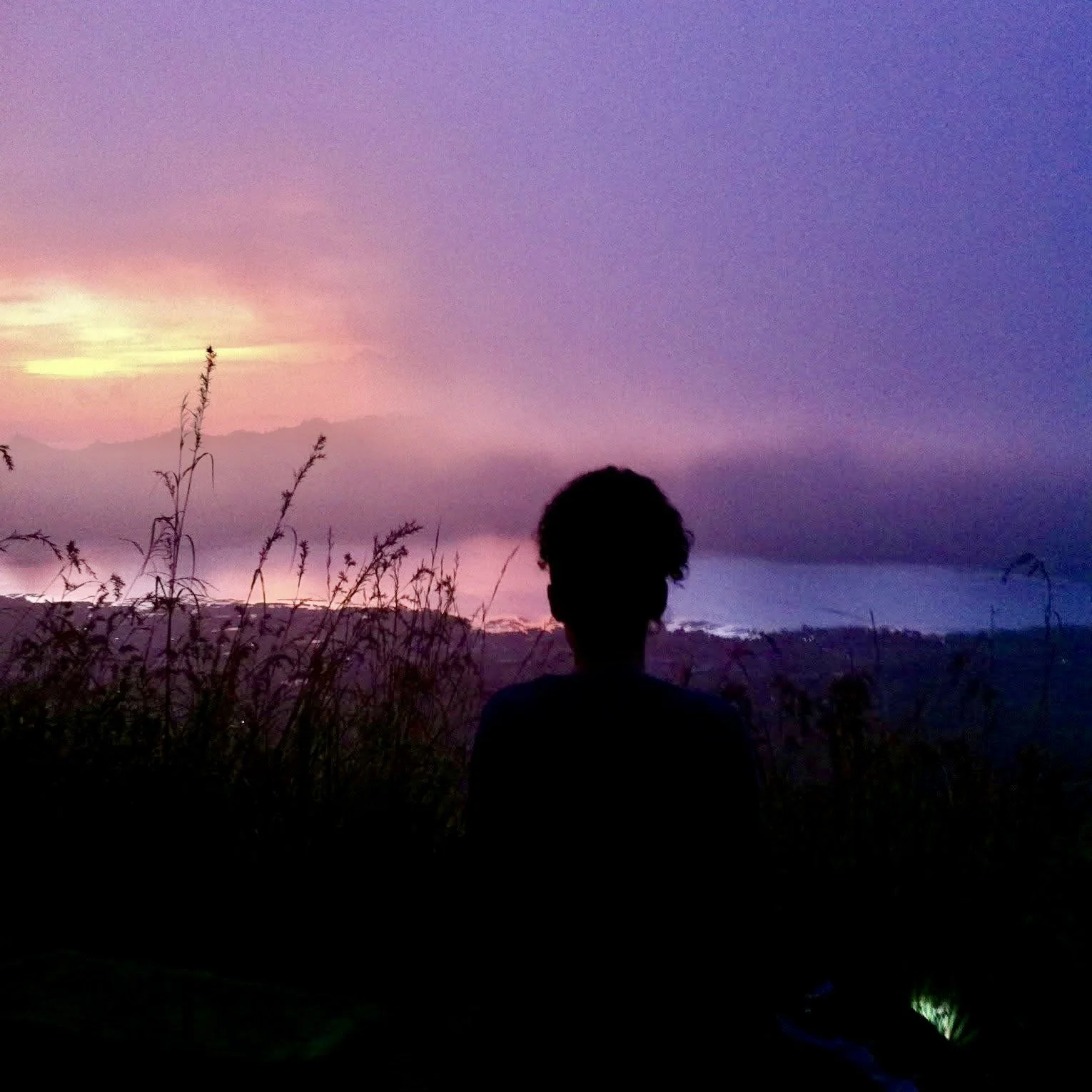 Silhouette of a woman looking out from the edge of a volcano at a pink and purple sunrise