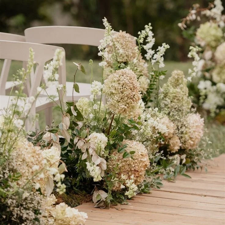 Beautiful cream and white hydrangea flower arrangements decorating a wooden pathway for an outdoor event.