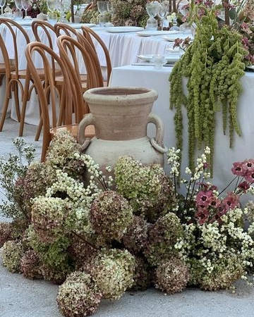 Large decorative vase surrounded by white, purple, and green hydrangea flowers at an outdoor event setup.
