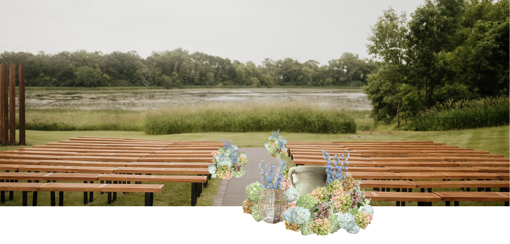 Empty wooden benches arranged outside near a lake with trees and wetland, decorated with floral arrangements and lanterns for an outdoor event.