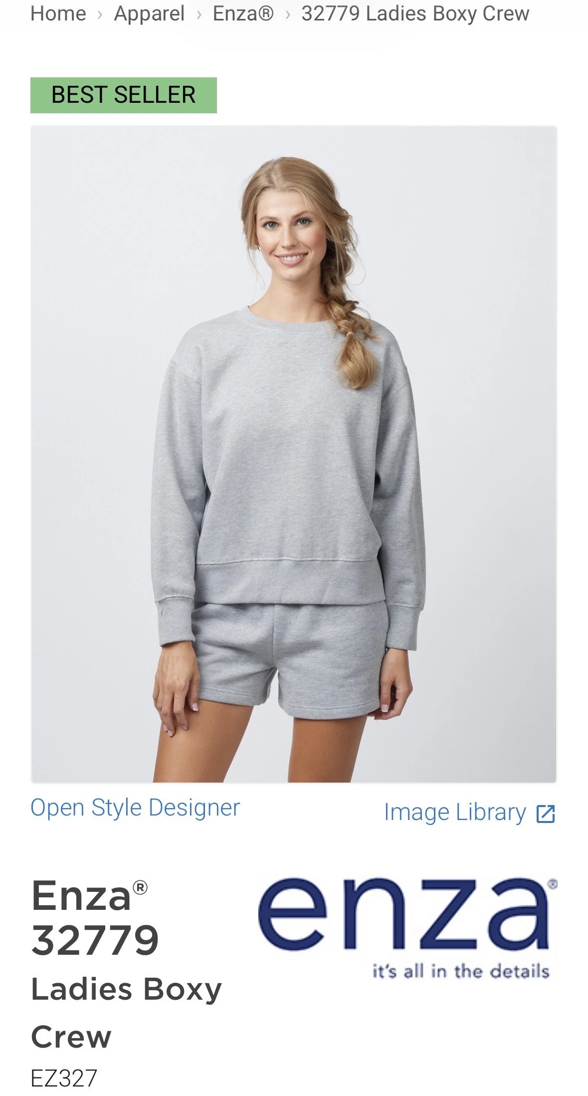 A woman wearing a gray sweatshirt and matching shorts, smiling at the camera, standing against a plain light background. commercial-work-hairstylist-book