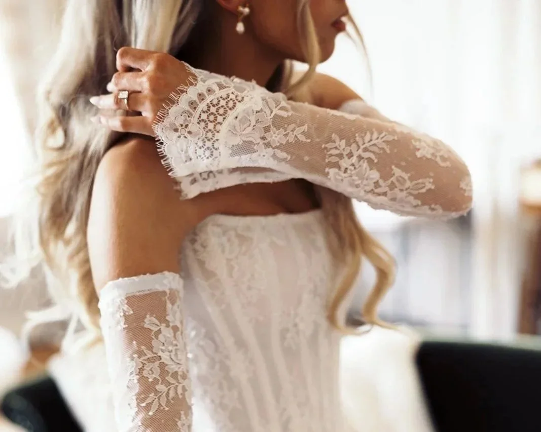 Close-up of a woman in a wedding dress with lace sleeves, adjusting her hair.