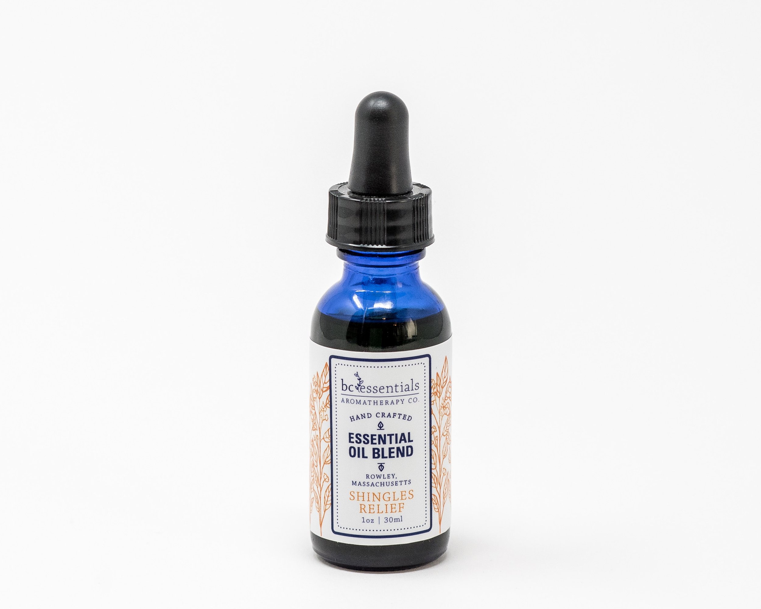 Dark blue glass essential oil bottle labeled 'Shingles Relief' on a light wooden surface