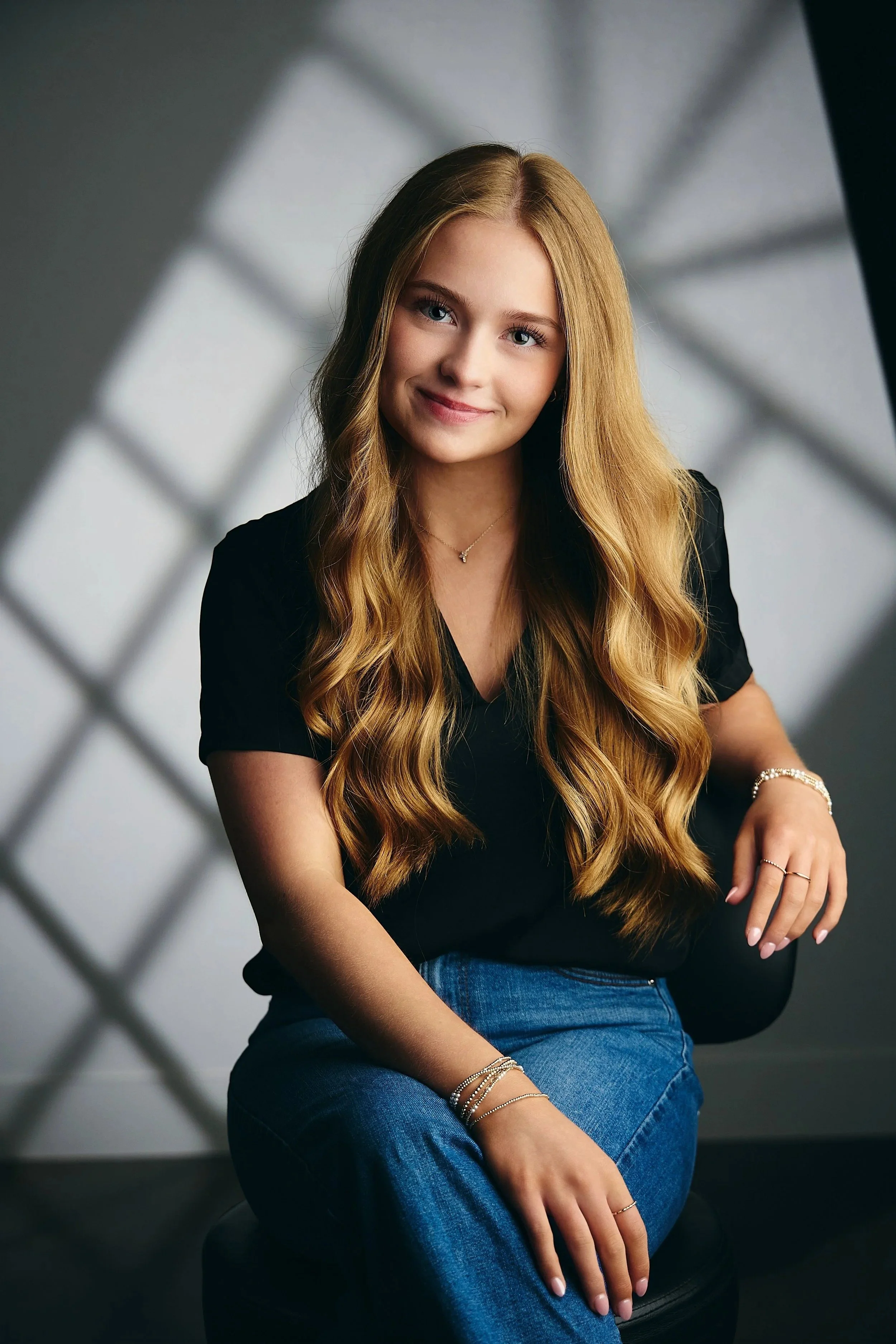 Senior picture pose: girl with long wavy hair seated in a black top and jeans