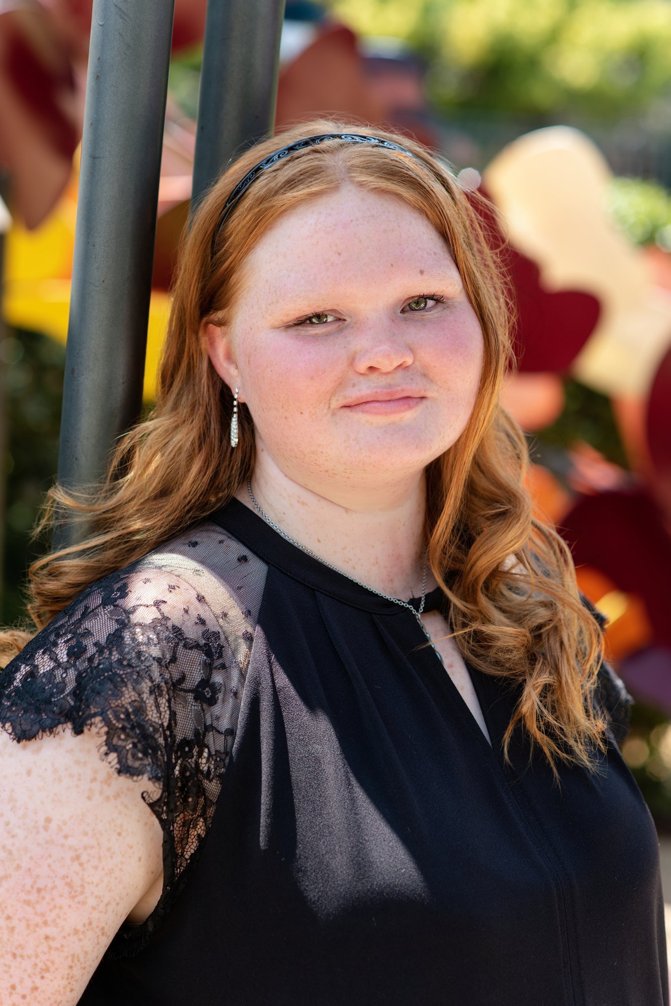 Senior portrait: girl with wavy red hair in a black lace-sleeve top among colorful flowers