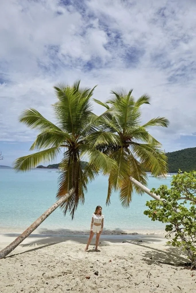 Senior picture outfit: girl standing on a sandy beach under leaning palm trees
