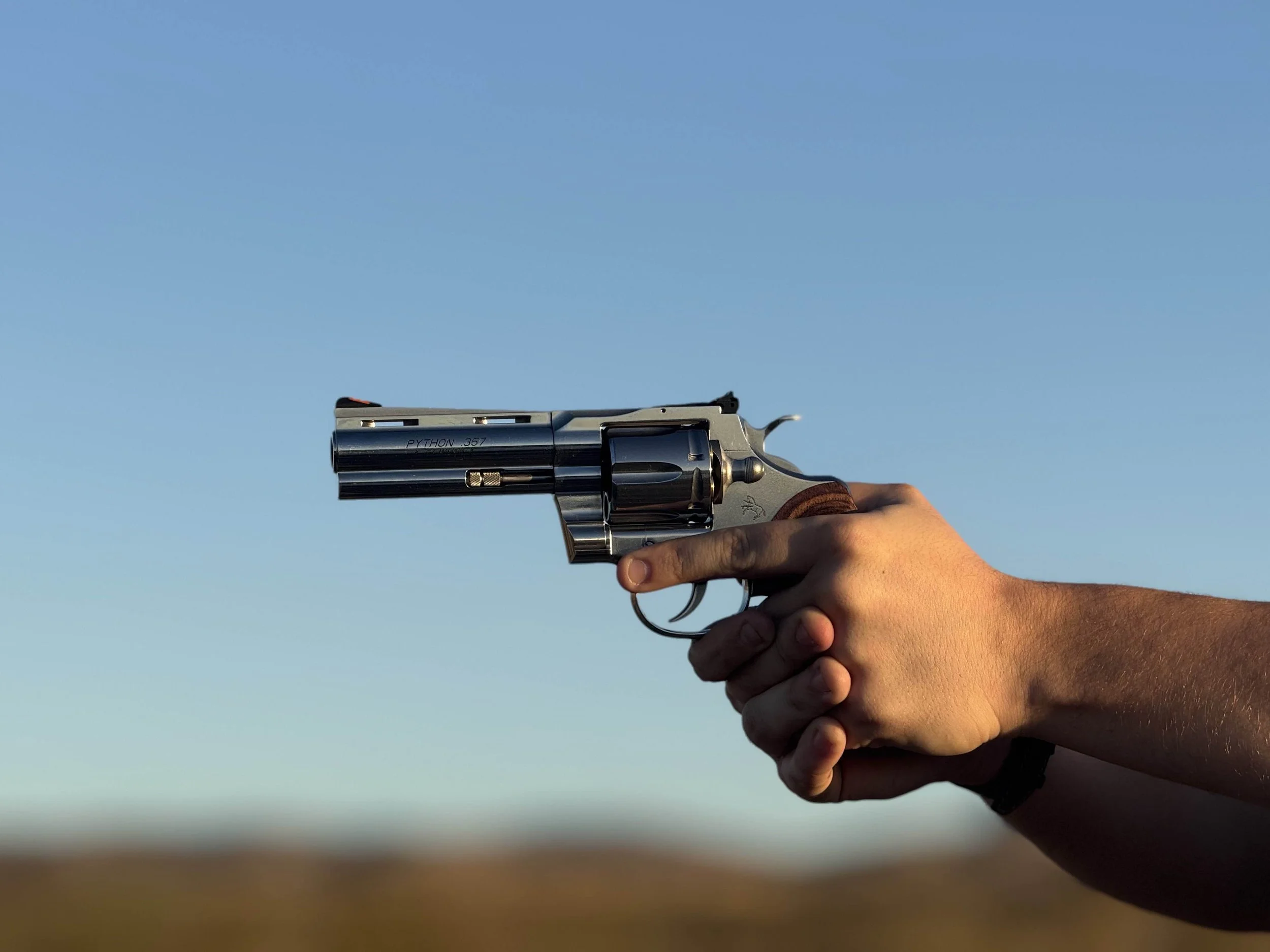 A person holding a silver revolver handgun with a clear blue sky in the background.