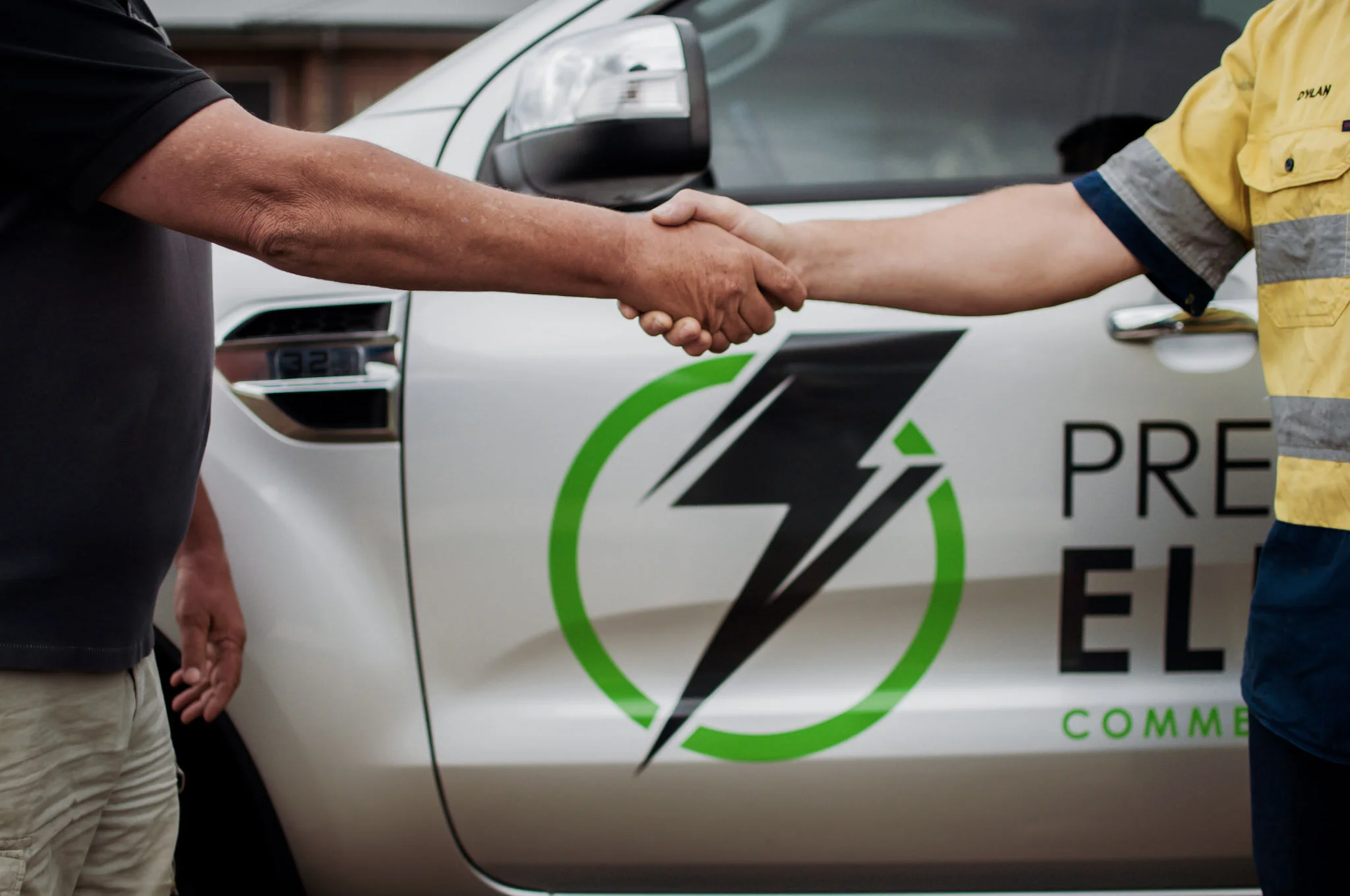 Two people shaking hands in front of a white vehicle with Precision Point Electrical branding on it.