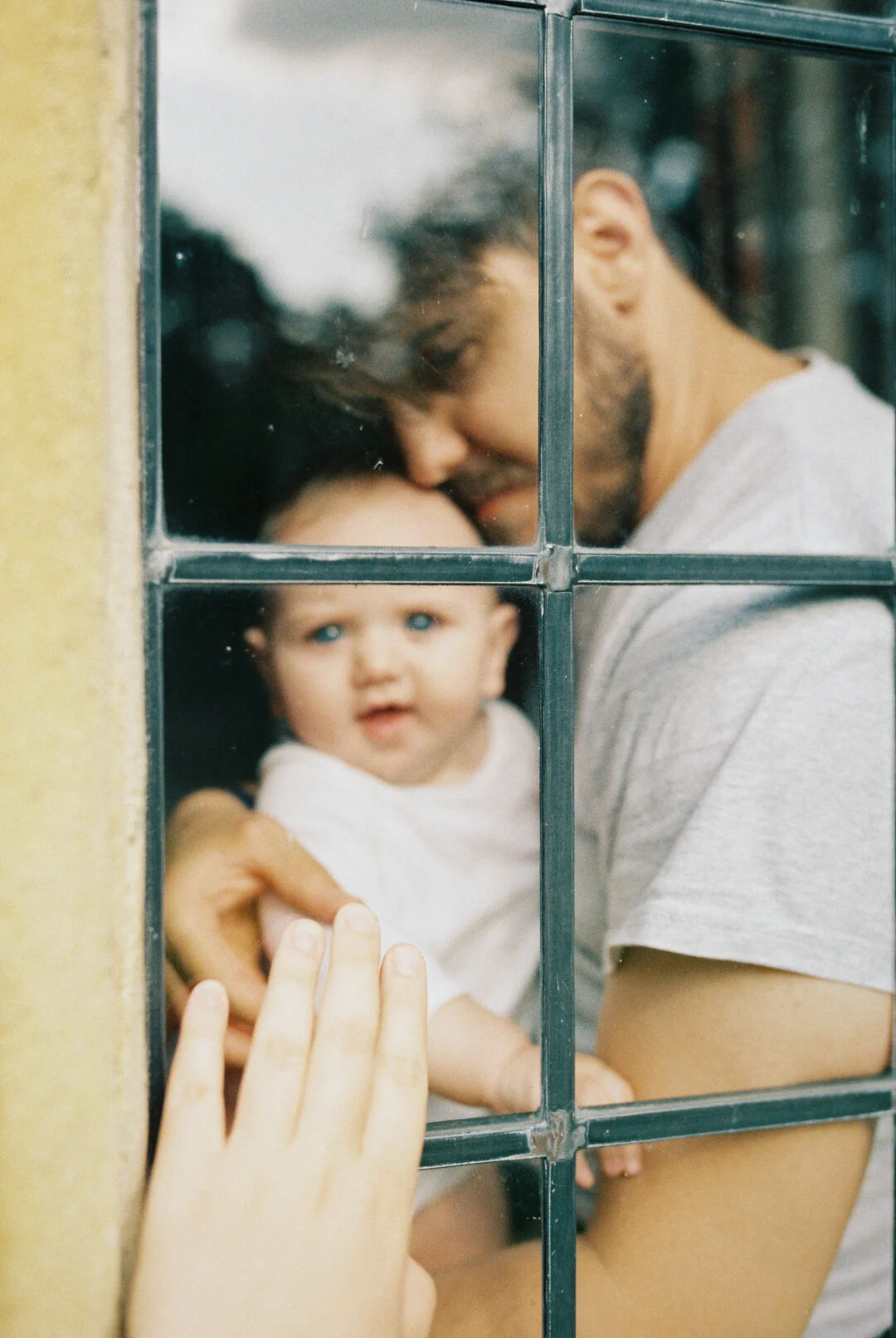 A father and a baby playing at home whilst mum looking at them taken during a family photoshoot in Hampstead