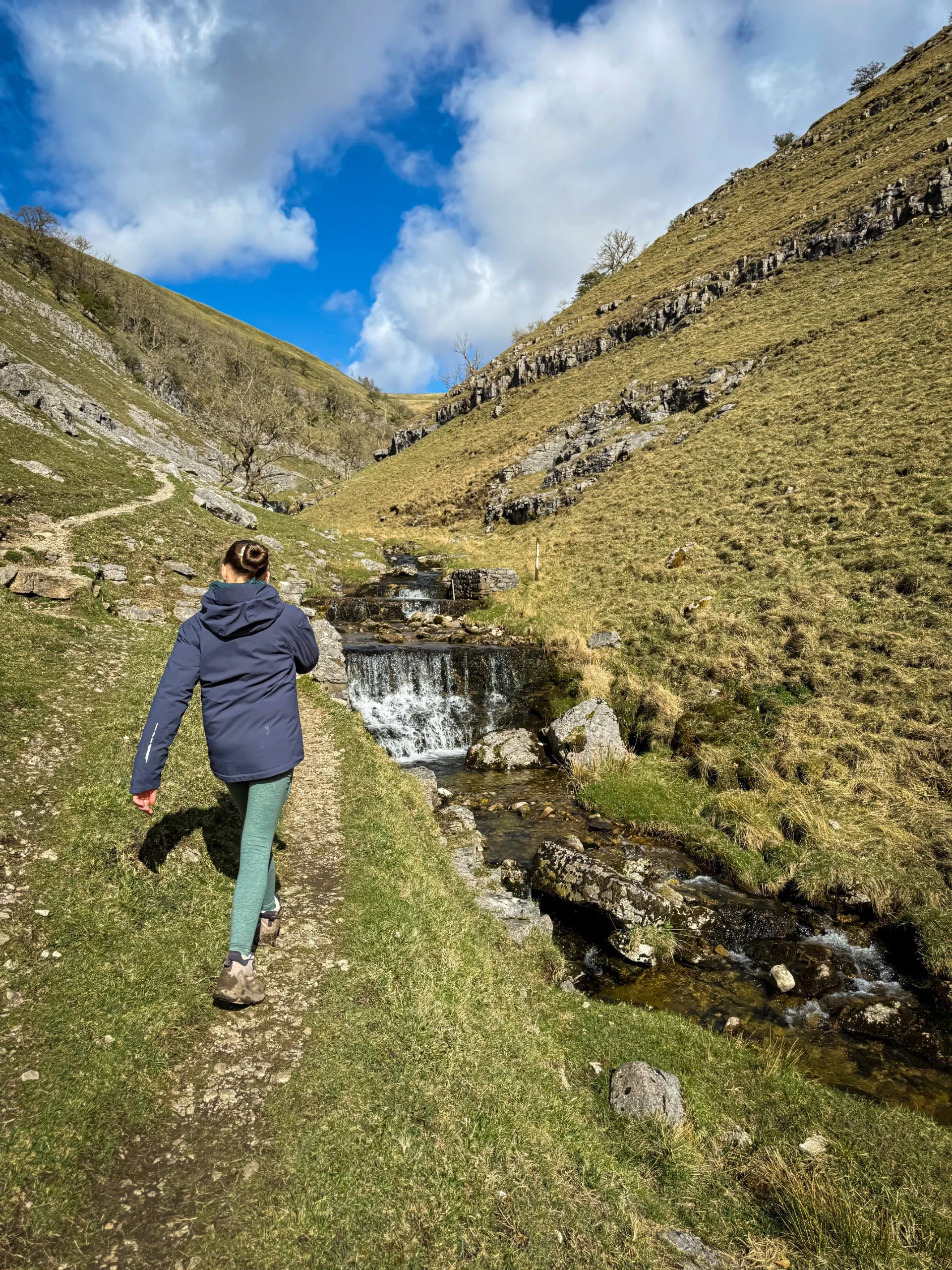 child walking along ravine under blue skies with cascading beck
