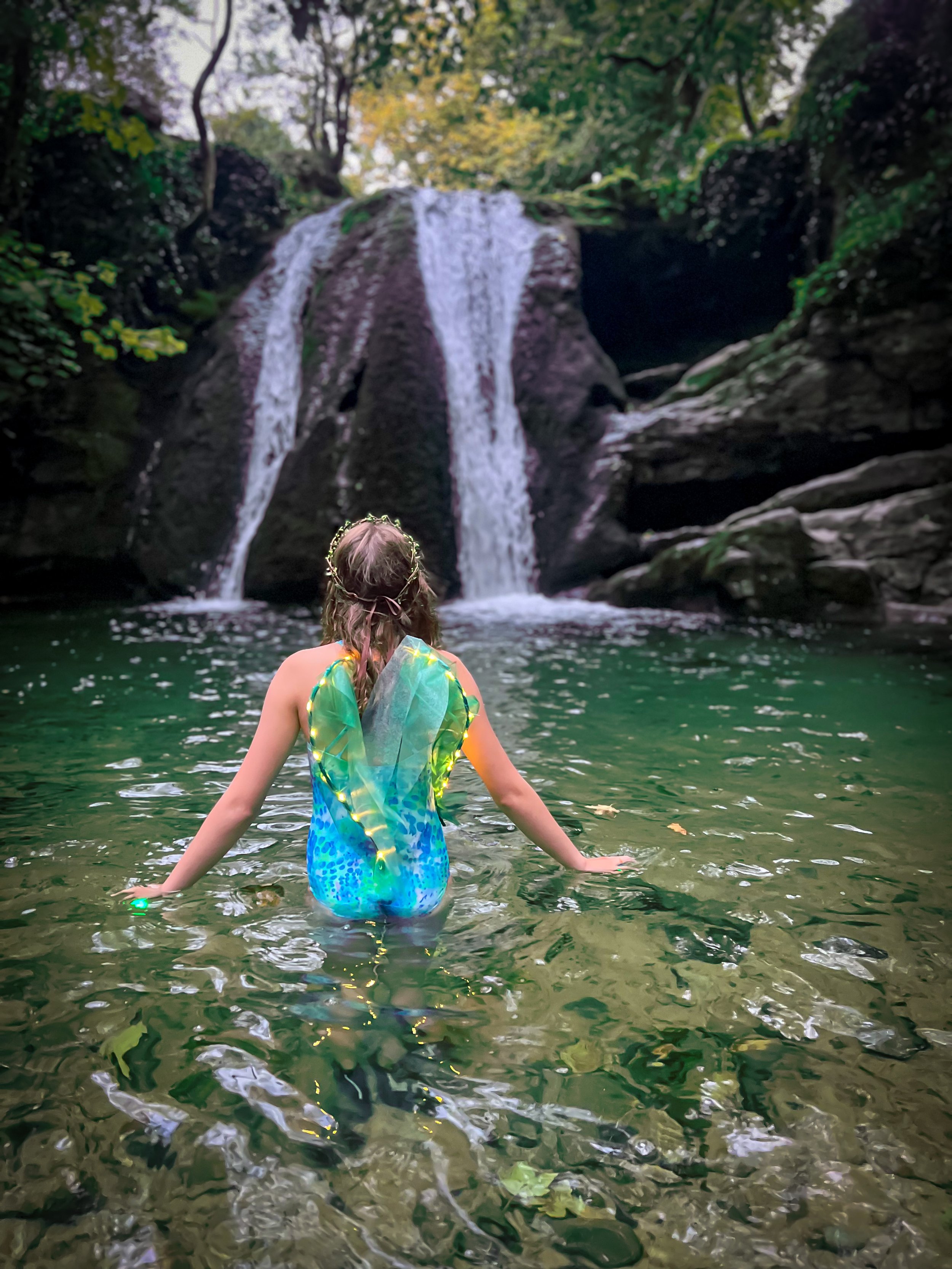 Child dressed as a fairy in  a waterfall
