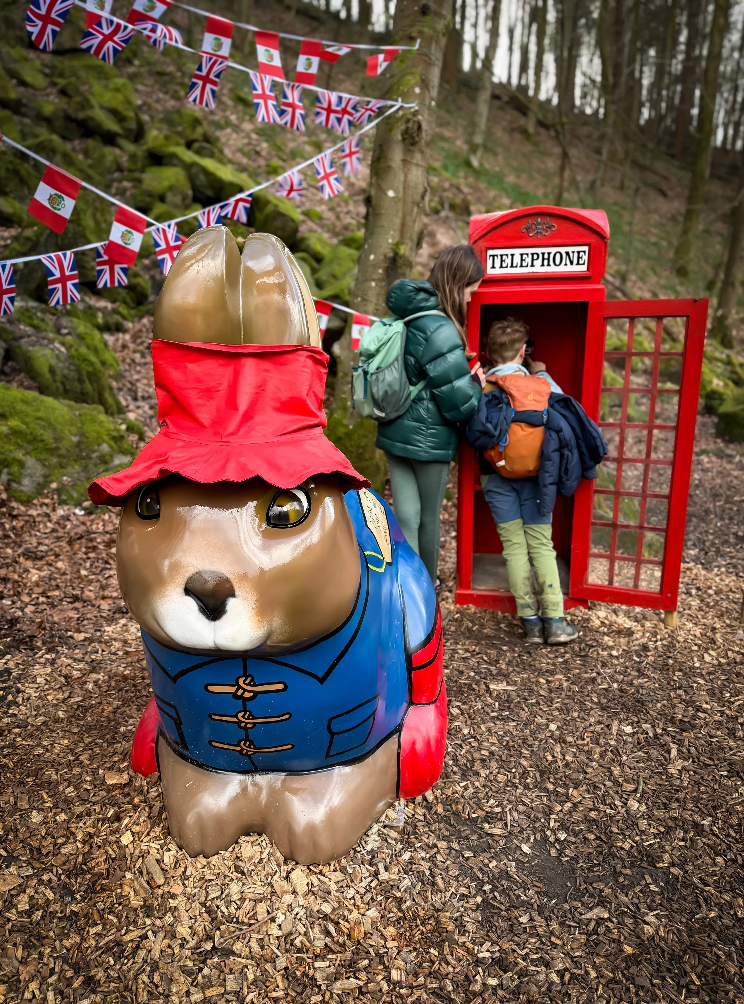 A giant paddington bear themed easter bunny in woodland with children behind