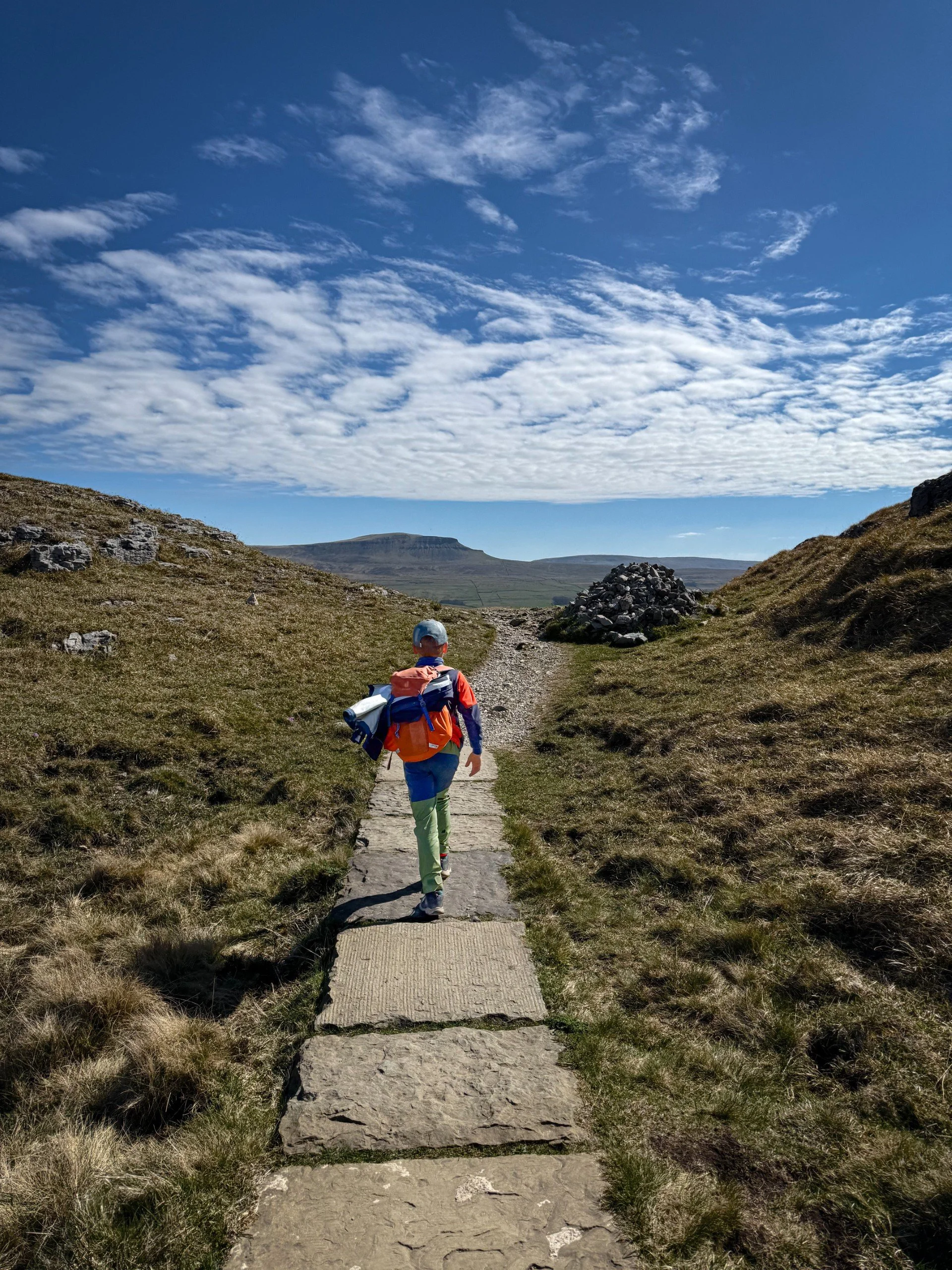 Child walking along flagged path with pen y ghent mountain in the distance and a large cairn under blue skies