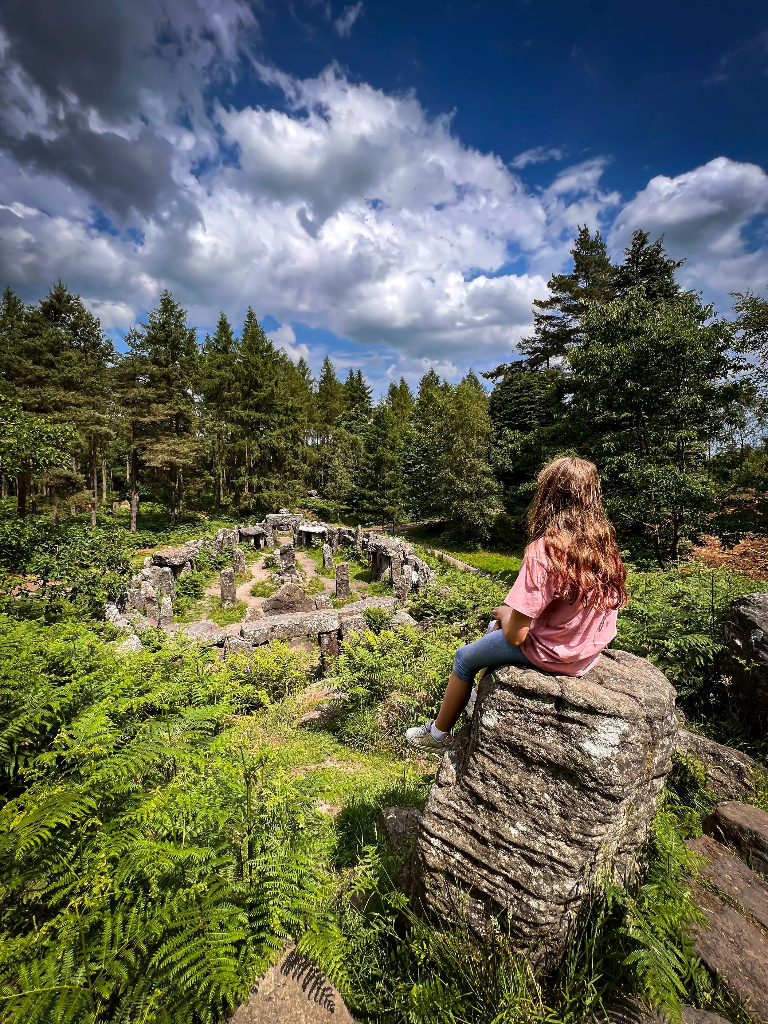 Children sitting overlooking the druids altar with trees, stone buildings and blue skies