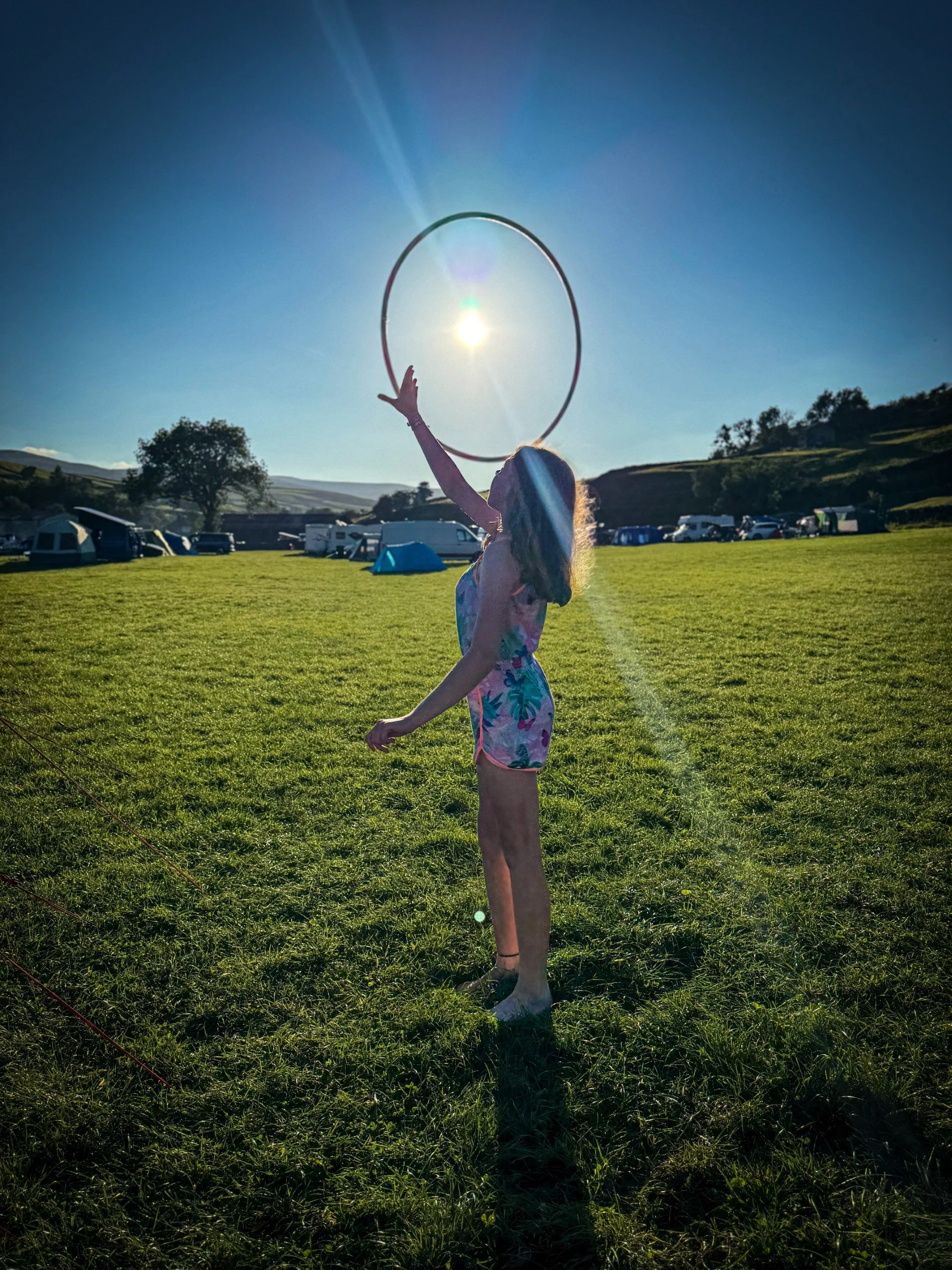 Child playing with a hoop with the sun shining through the centre of it on a campsite