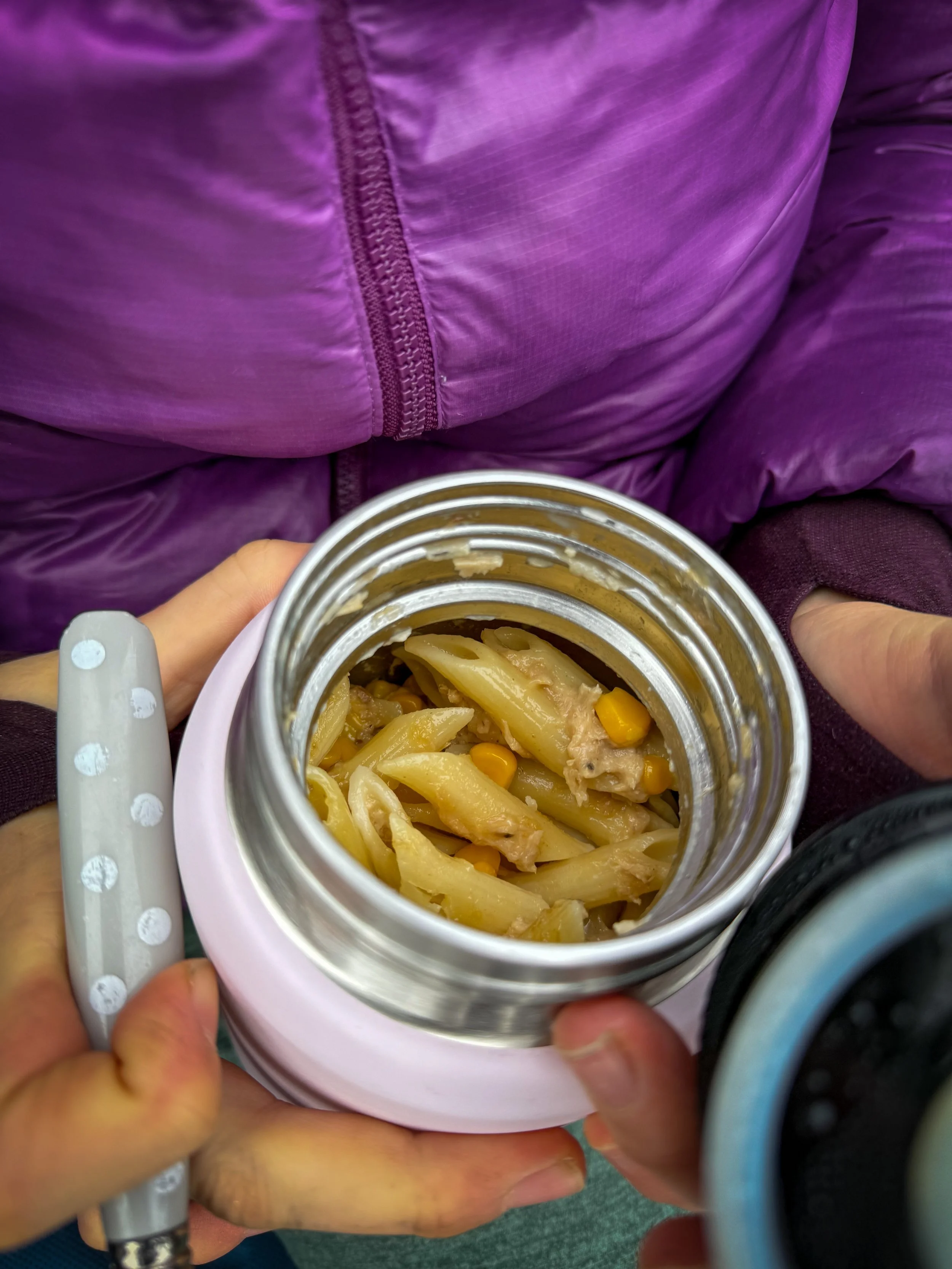 Child in a purple coat with a flask of food in her hands