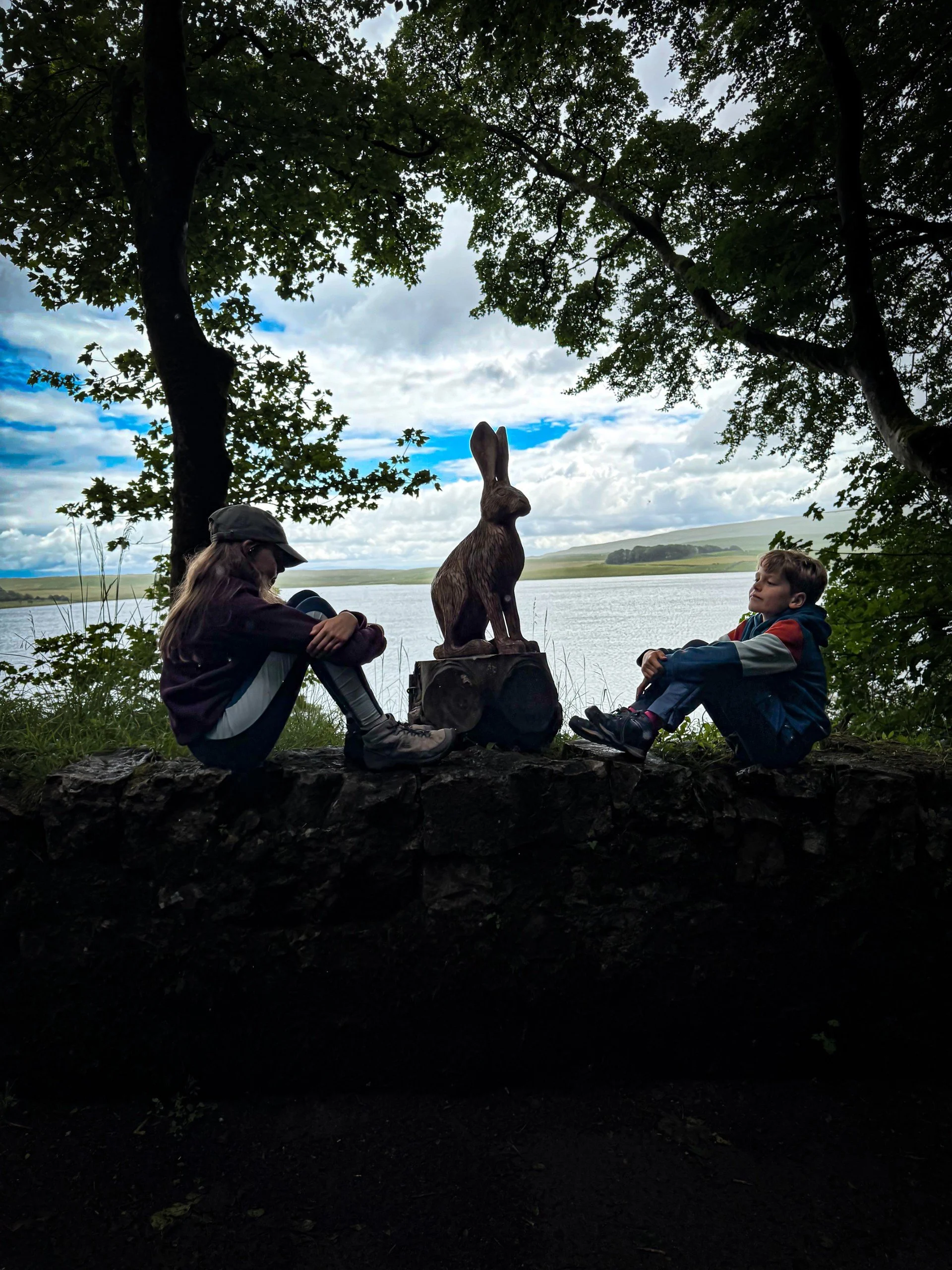 Two children sitting alongside a rabbit sculpture