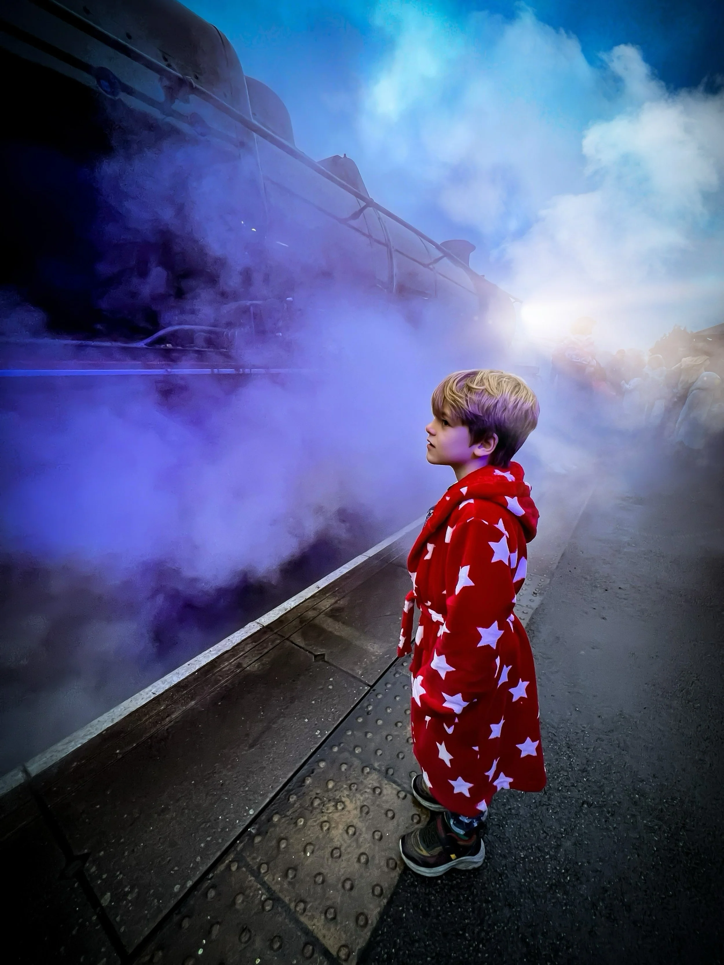 Child standing in red starry dressing gown next to a large steam train