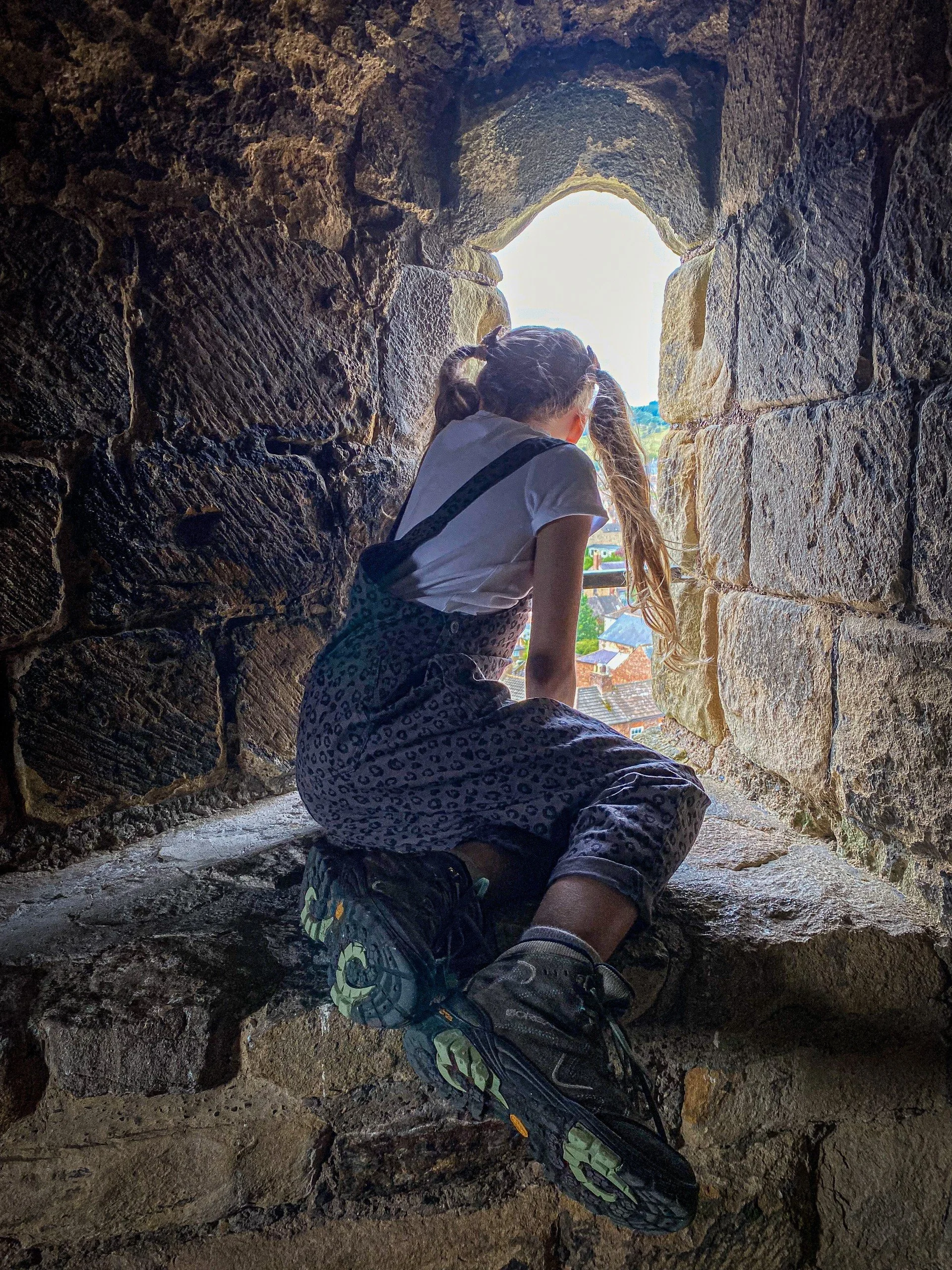 Child sat in a window of a castle wearing dungarees and bunches