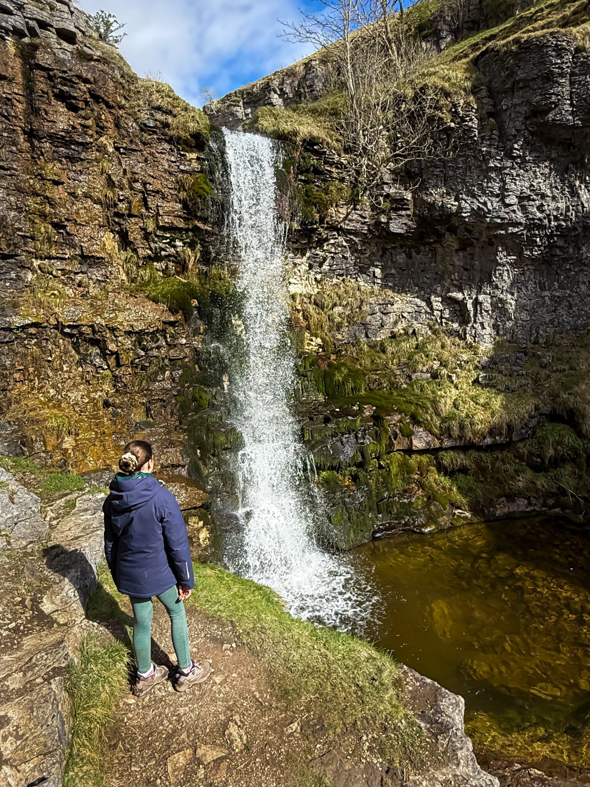 Child standing in front of tall waterfall in spring
