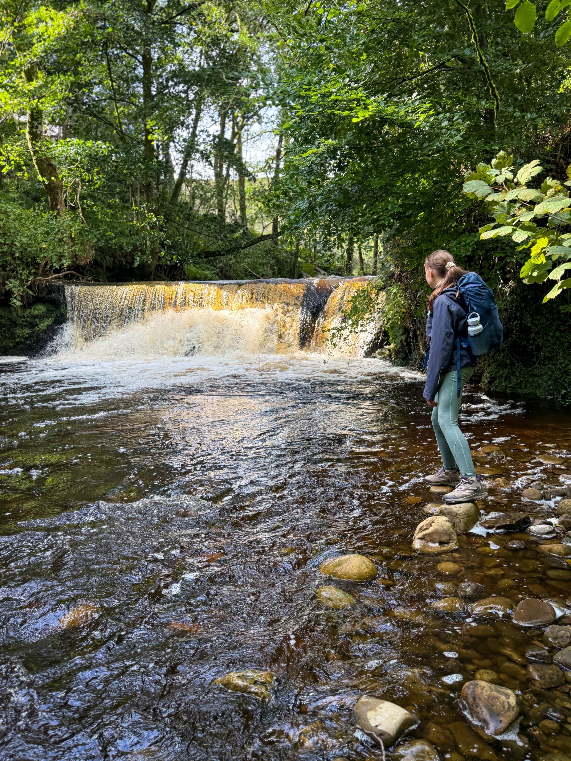 Child standing next to a waterfall in late summer woodland