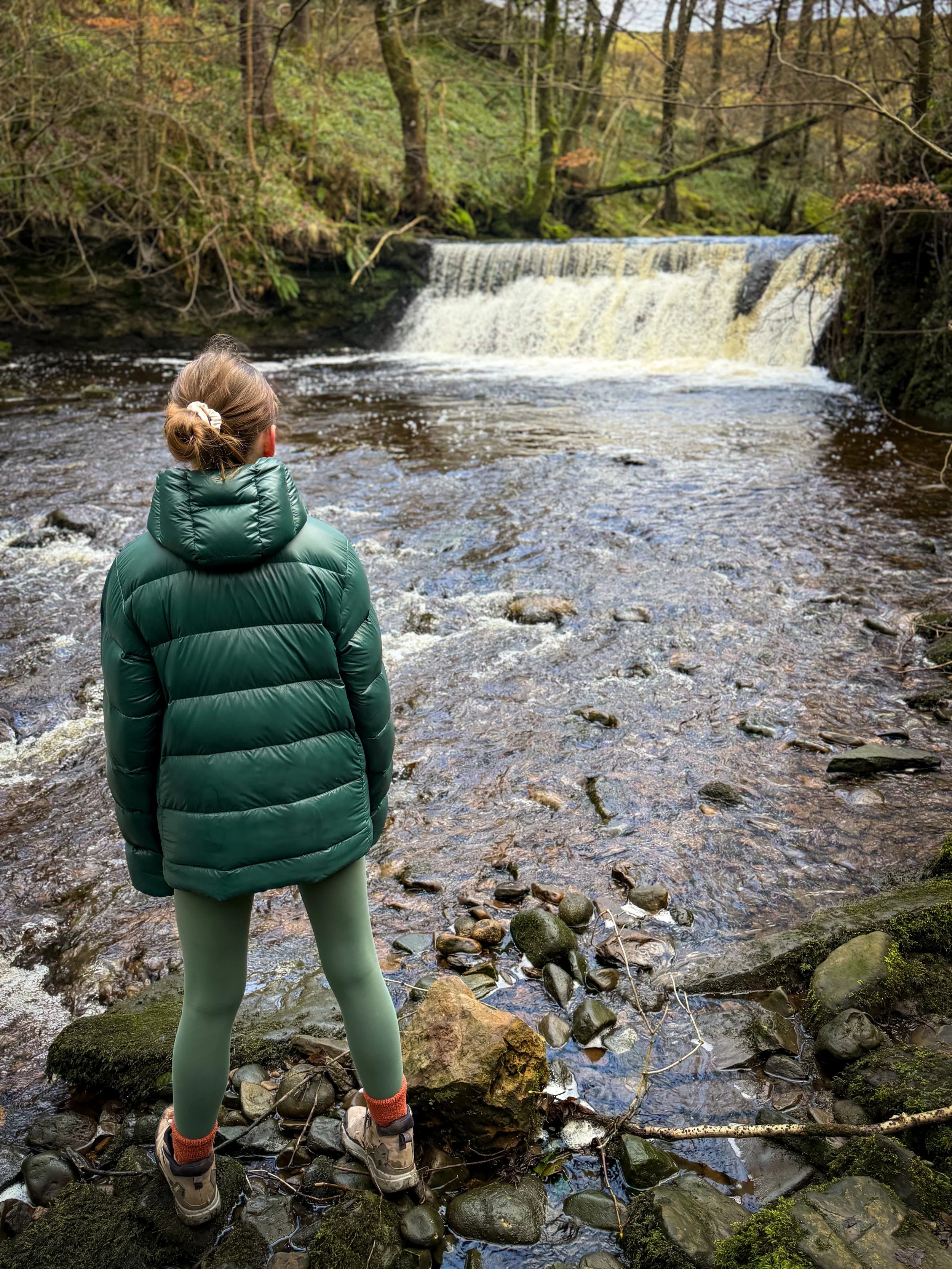 Child standing in front of waterfall in winter wearing green coat