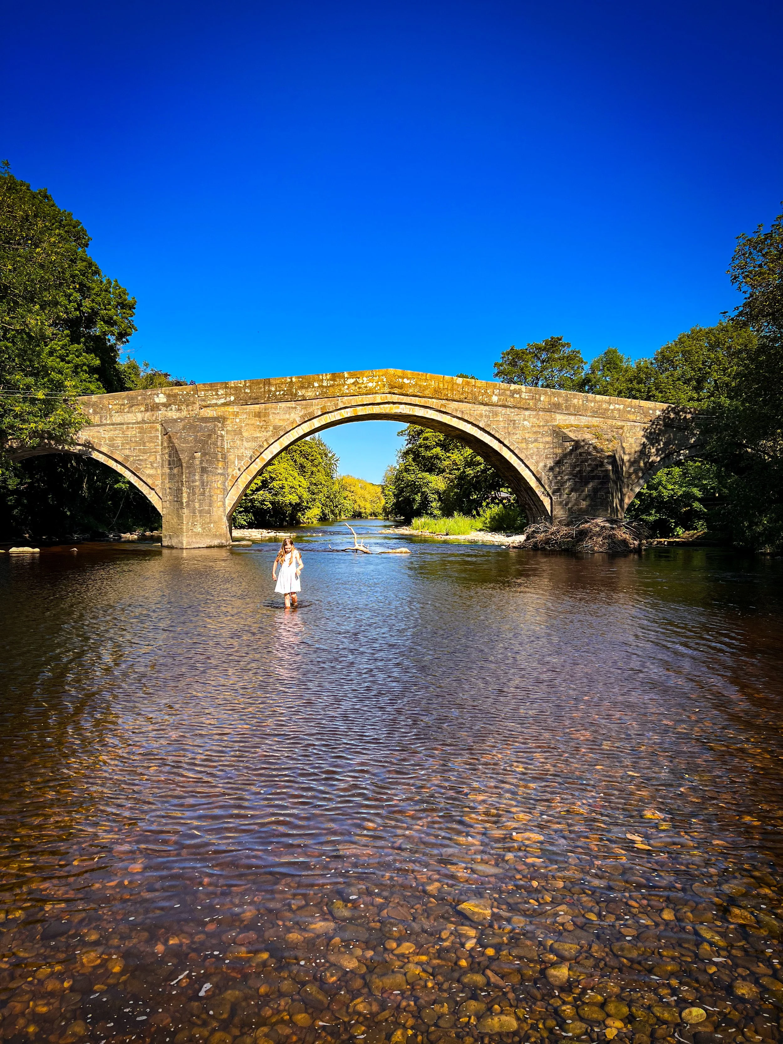 Child walking in water in front of a stone bridge