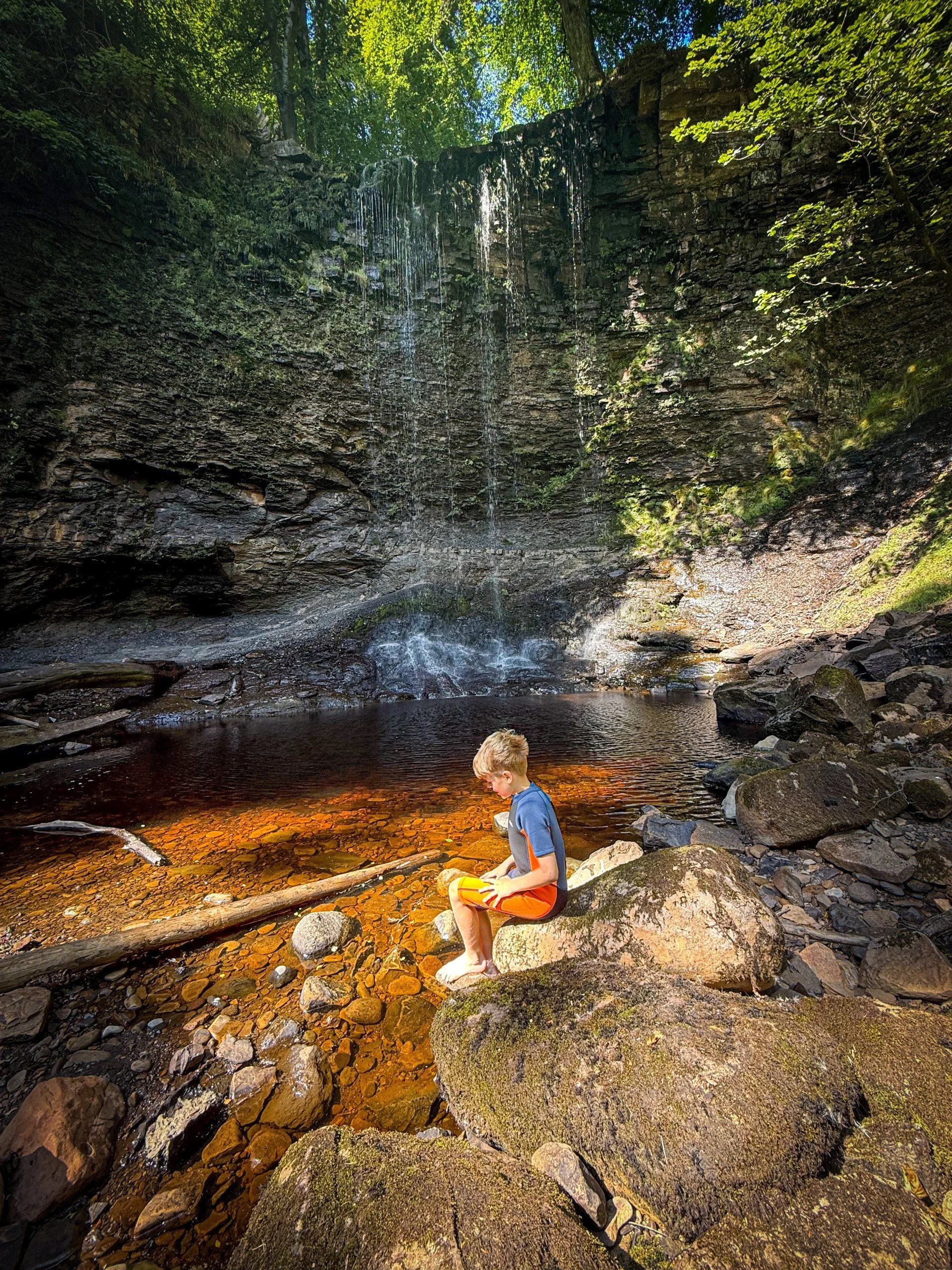 Child sat next to a waterfall in the high Summer sun