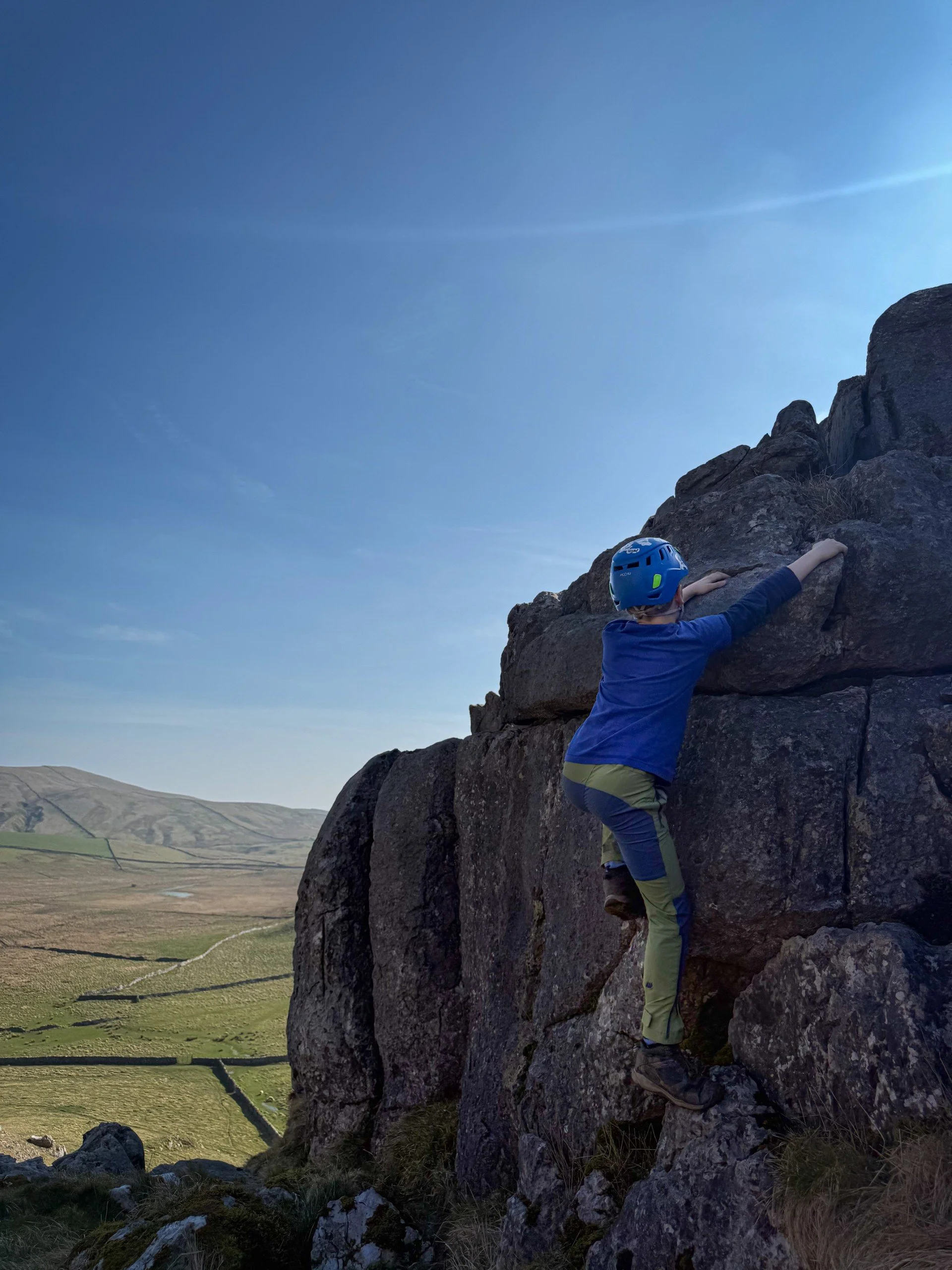 Kid climbing up a rock wearing climbing helmet under blue skies