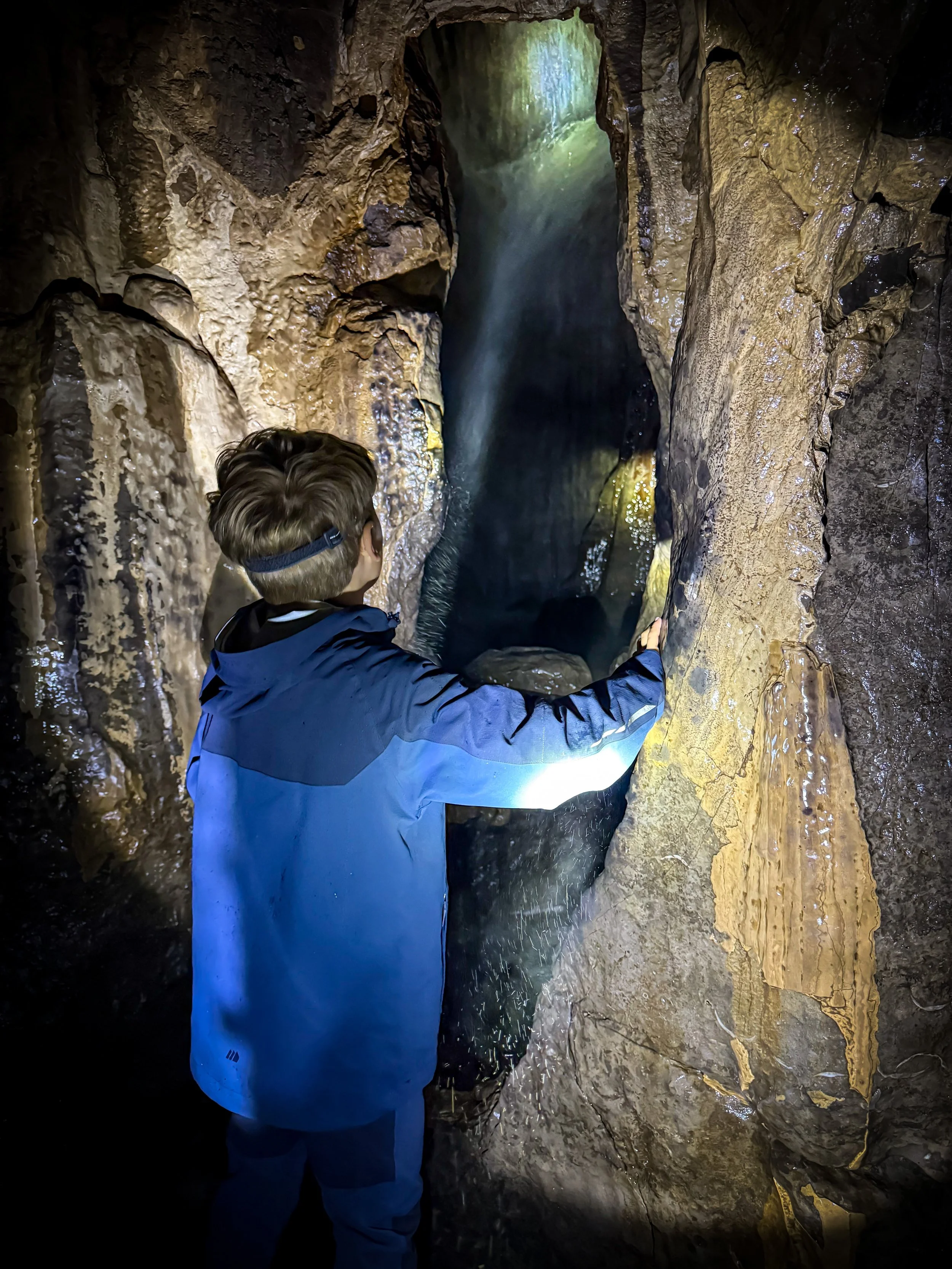 Child standing with headdtorch looking into a cave with a waterfall in the dark
