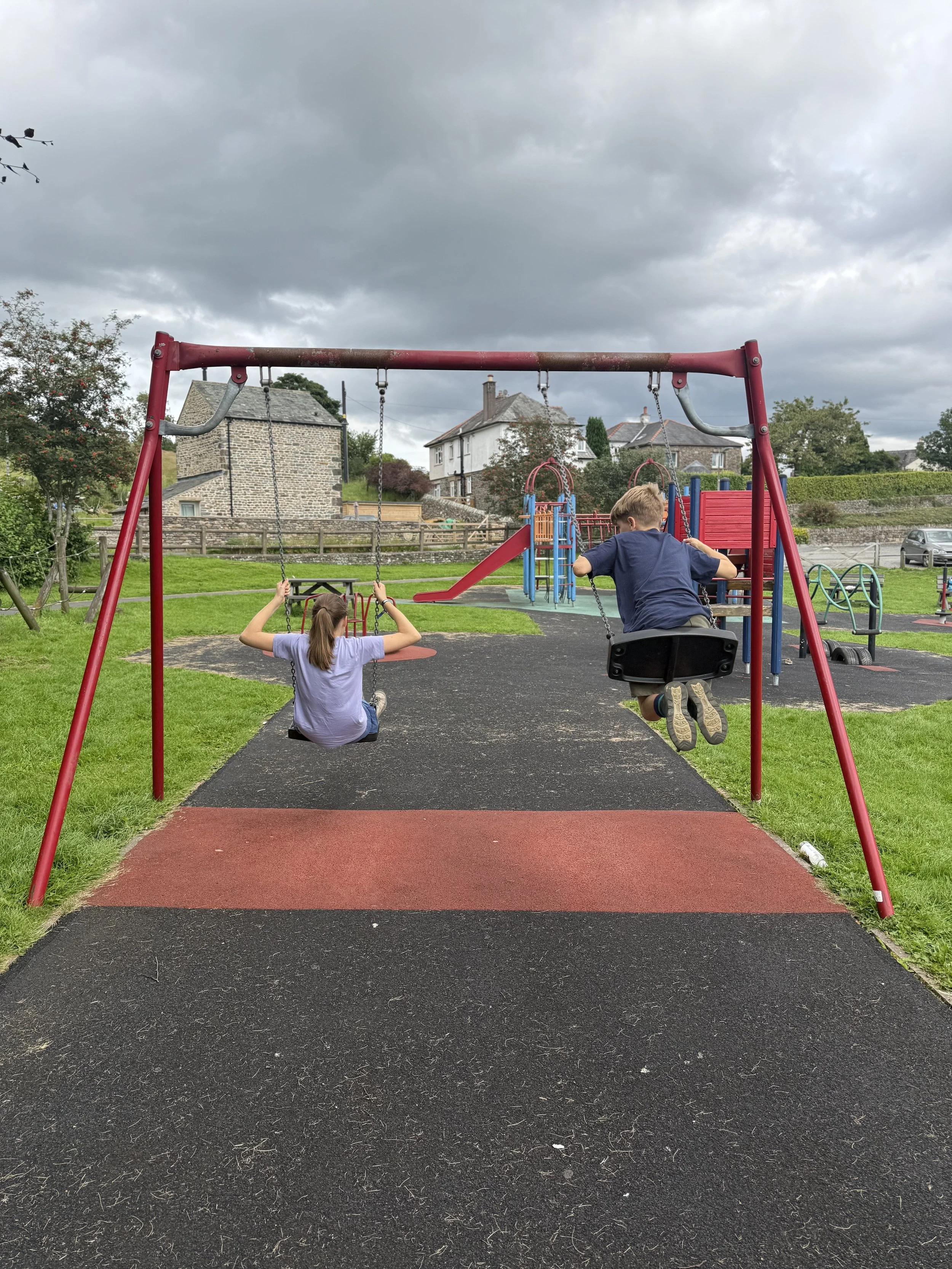 Children swinging on swings with houses behind and play park
