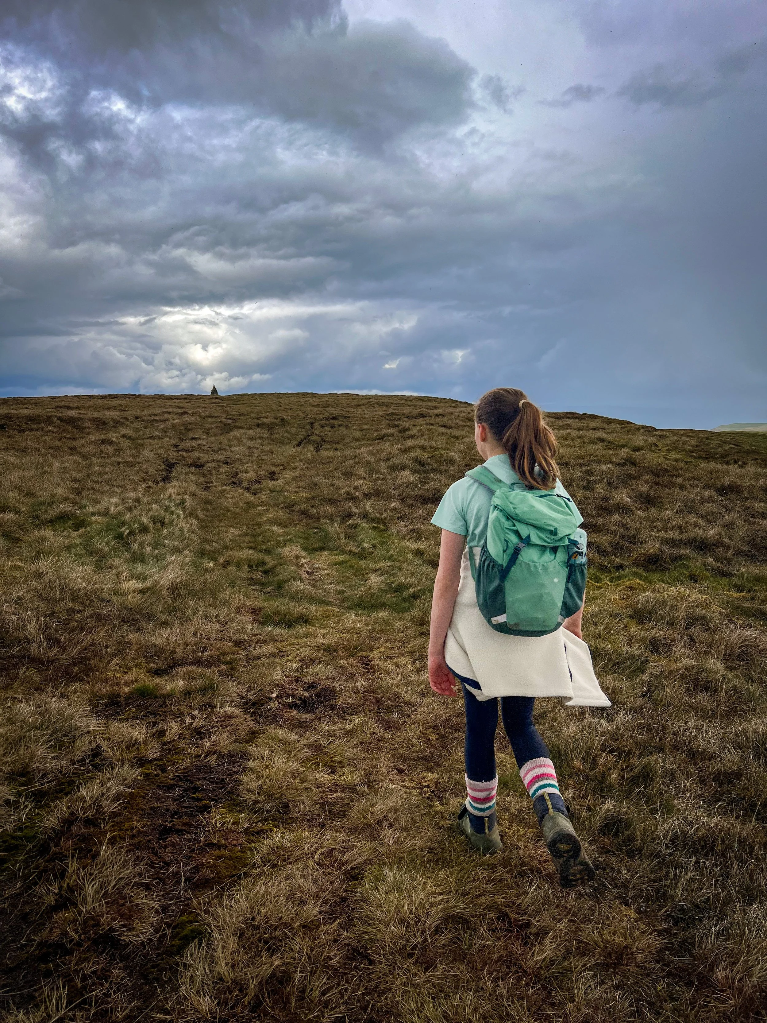 Child walking towards summit cairn with light in clouds