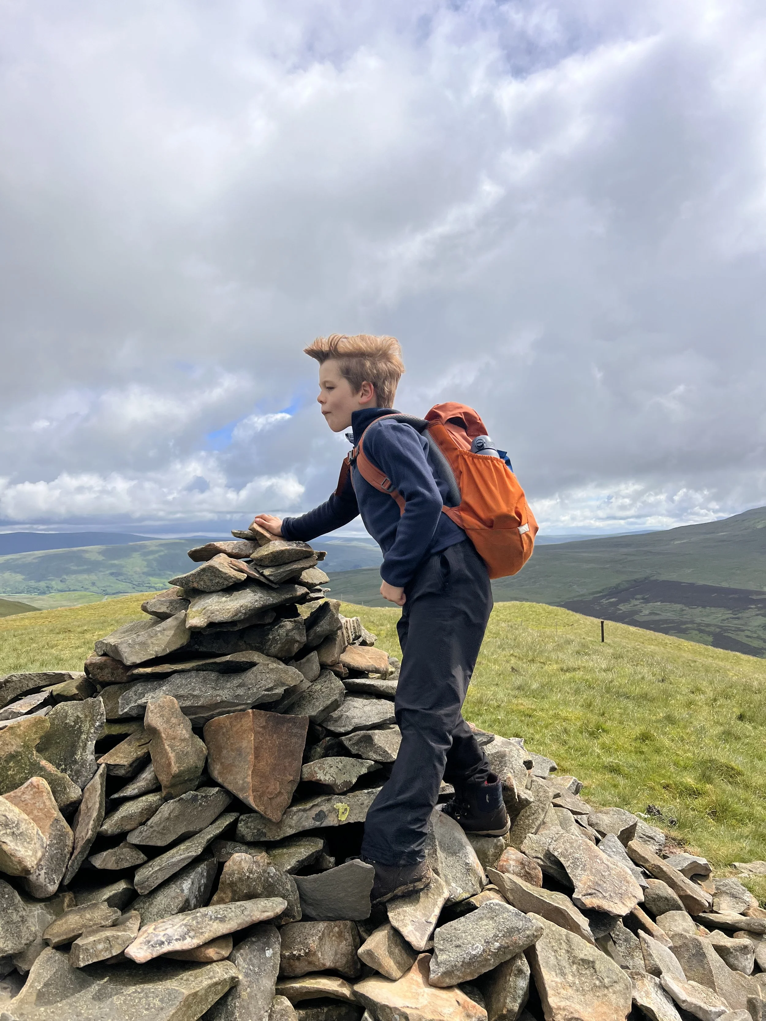 Child standing at a mountain cairn with mountains behind