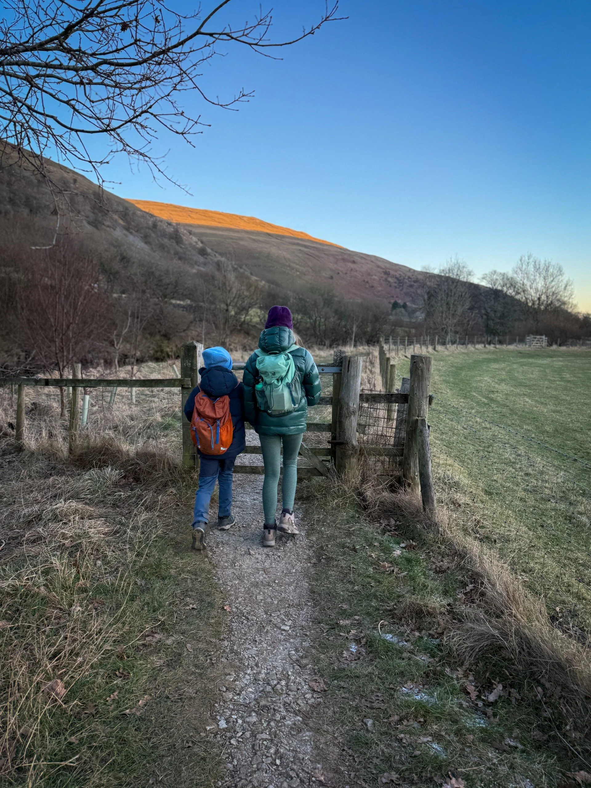 Two children walking along a stony path with big hills to the left with late evening sun on the hillside