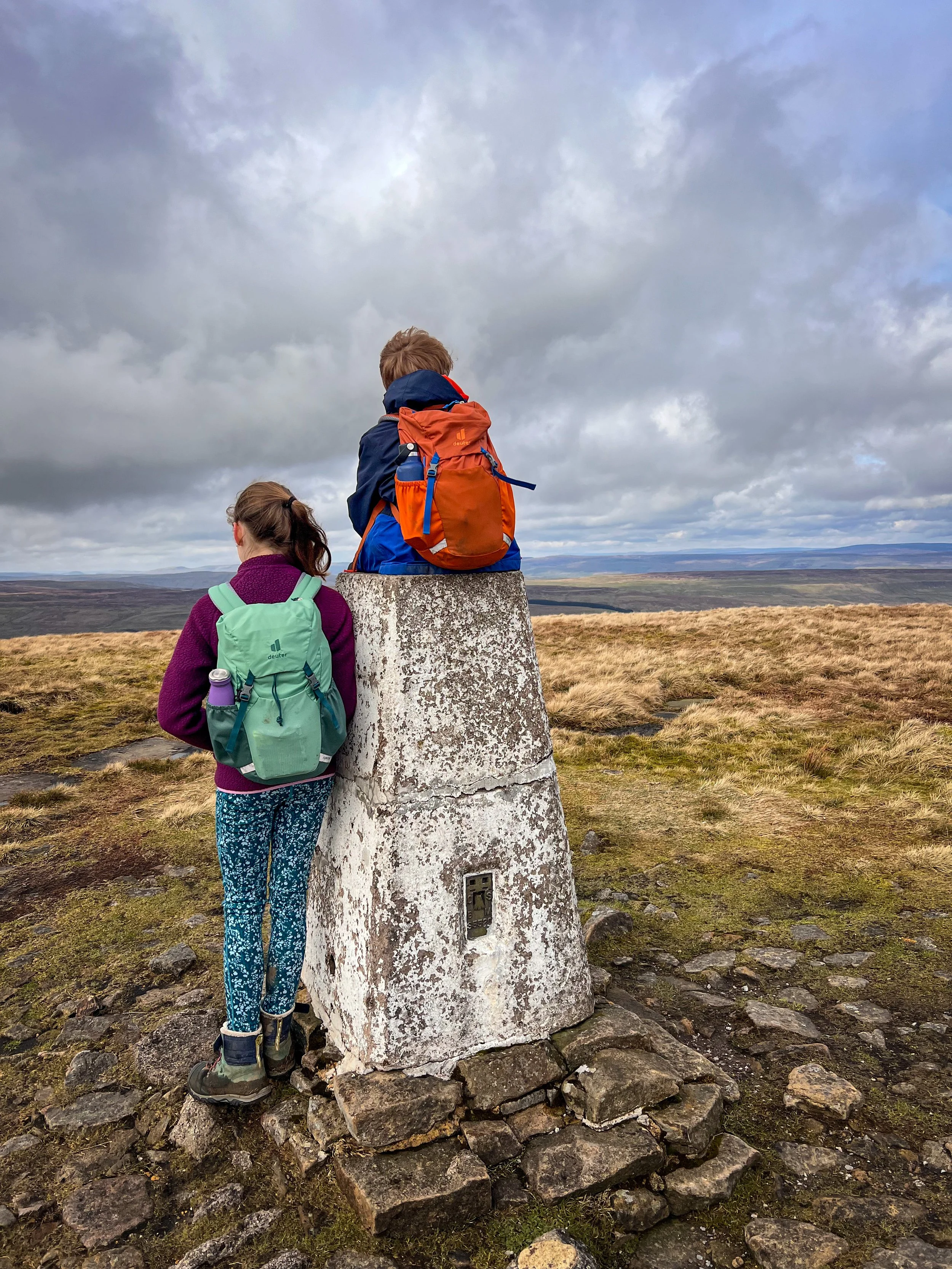 Two children sat on a trig point on top of a mountain