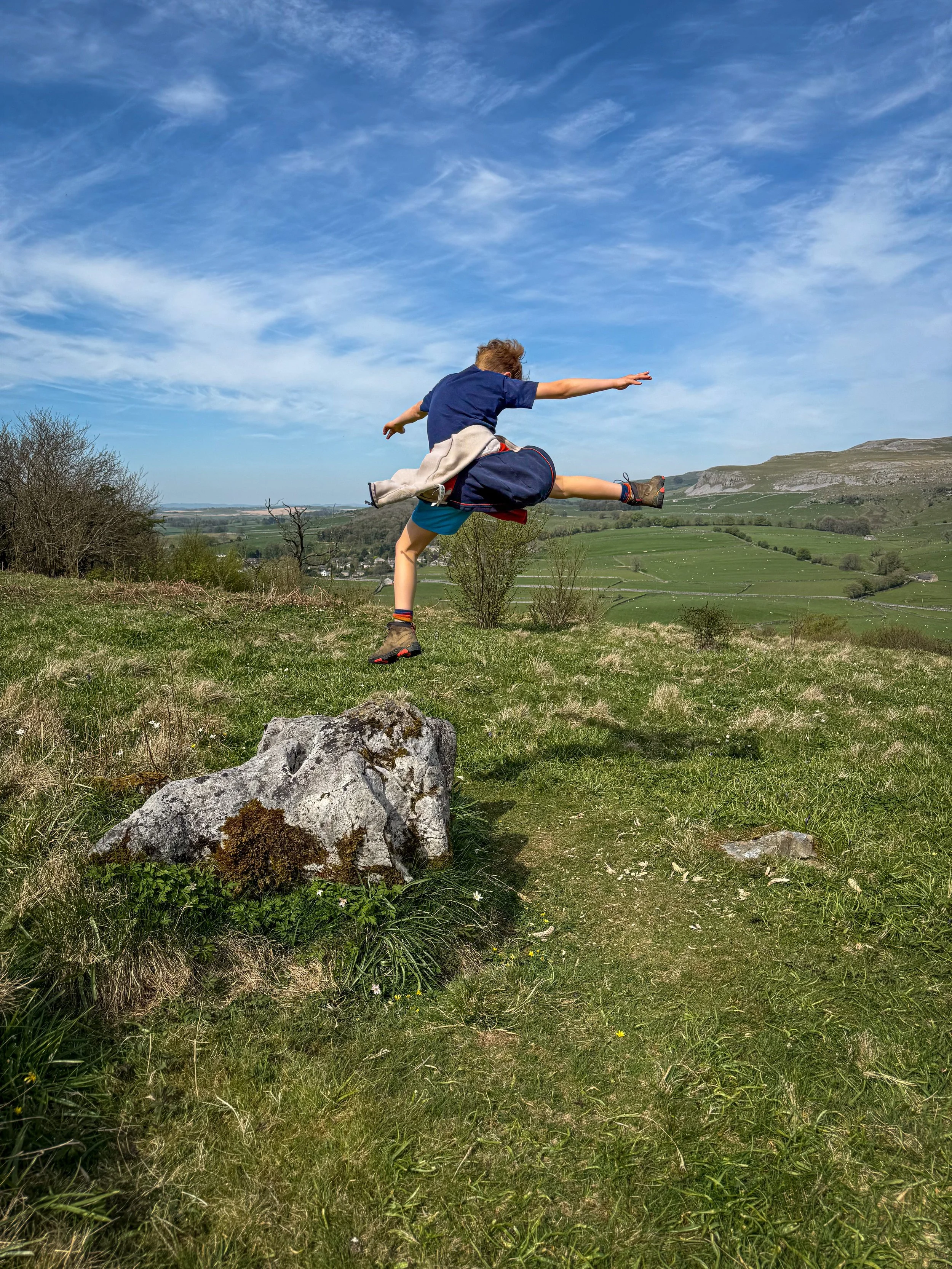 Child jumping off a rock with blue sky behind