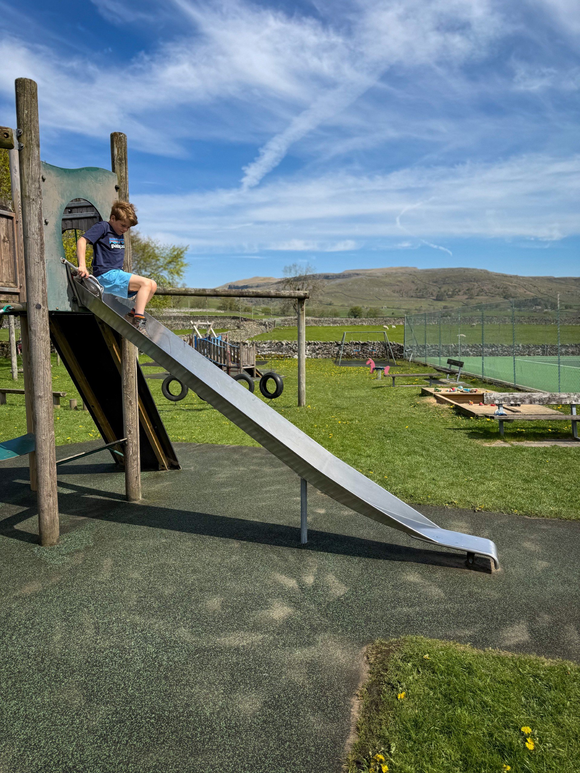 The slide at Austwick play park with hills and sandpit and obstacle course behind