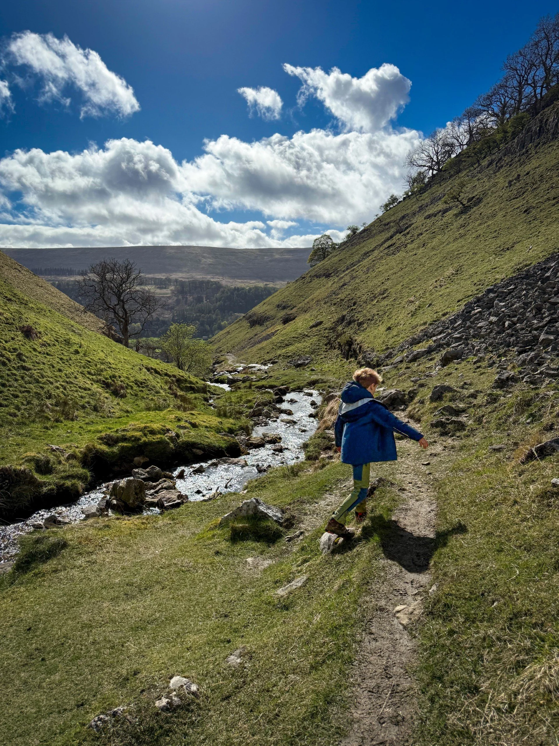 Child walking down a path next to a beck under blue skies with fluffy clouds