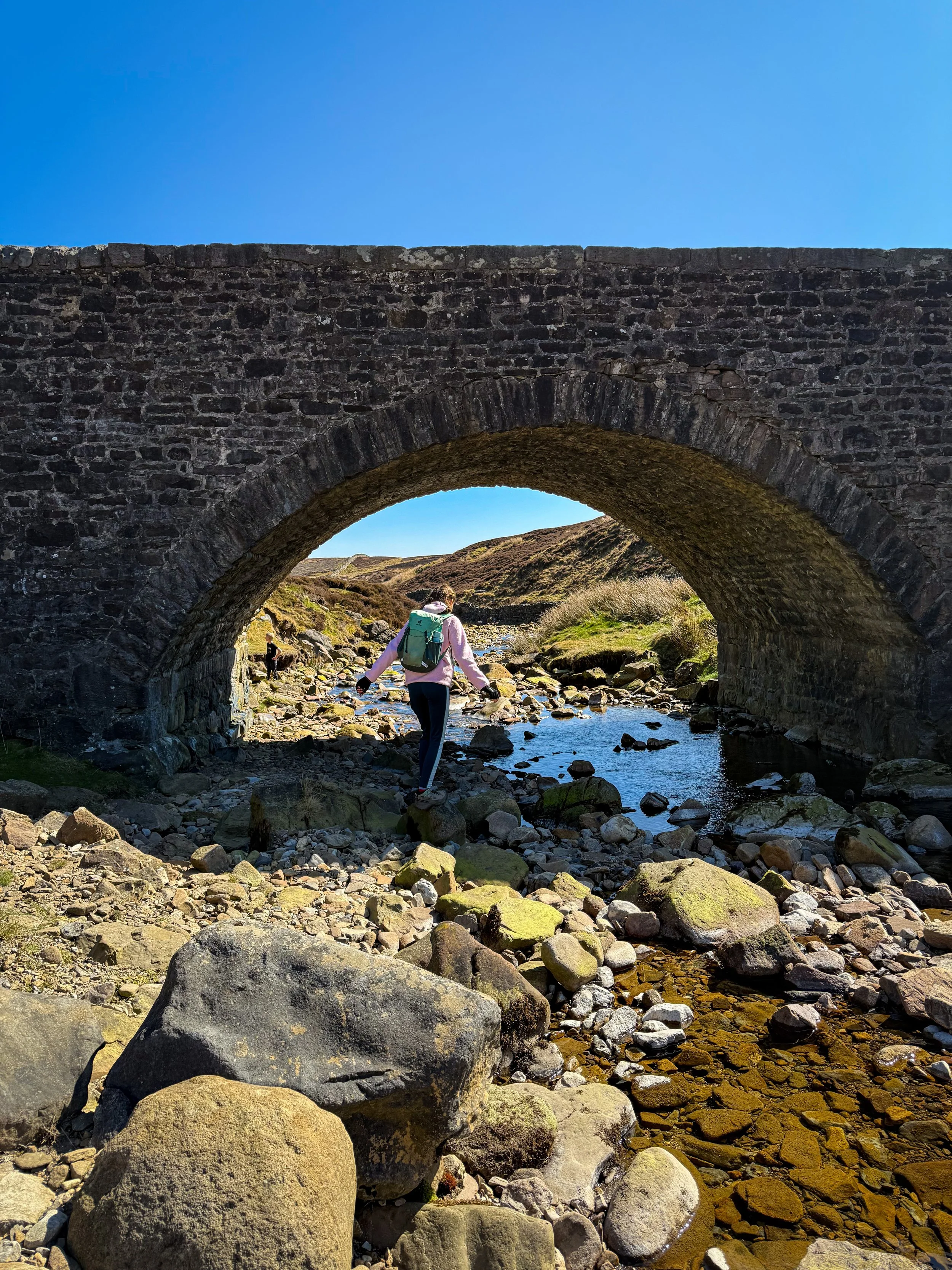 child playing in the water under the a dry stone bridge