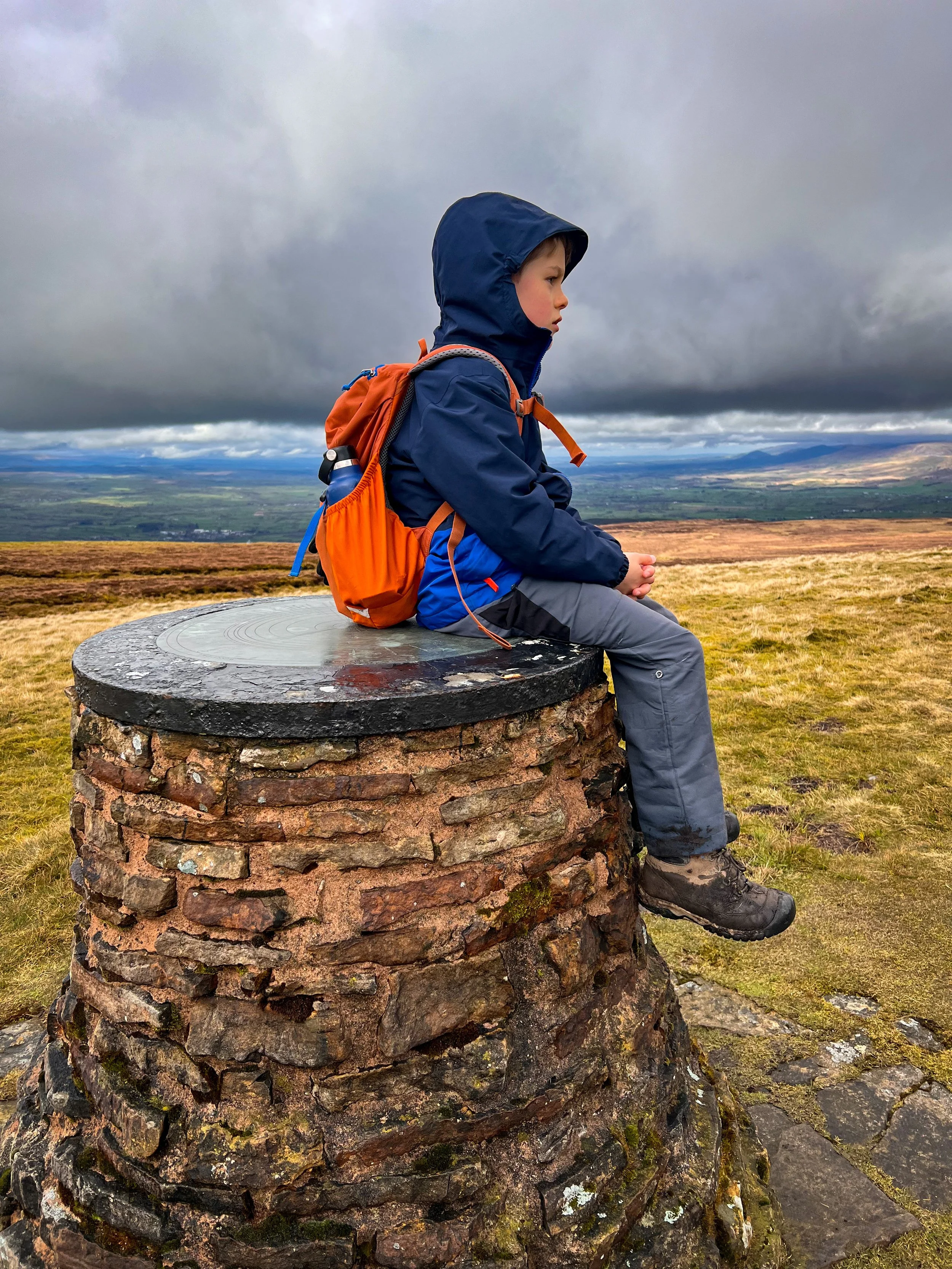 Child sat on top of a view point with clouds and mountains in the distance