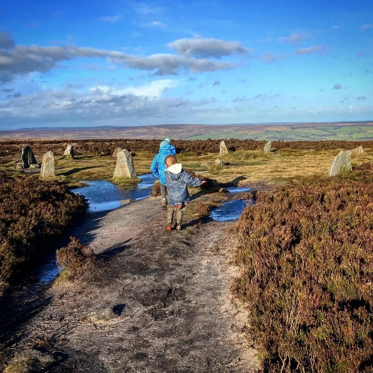 Children walking into a stone circle with blue skies and puddles