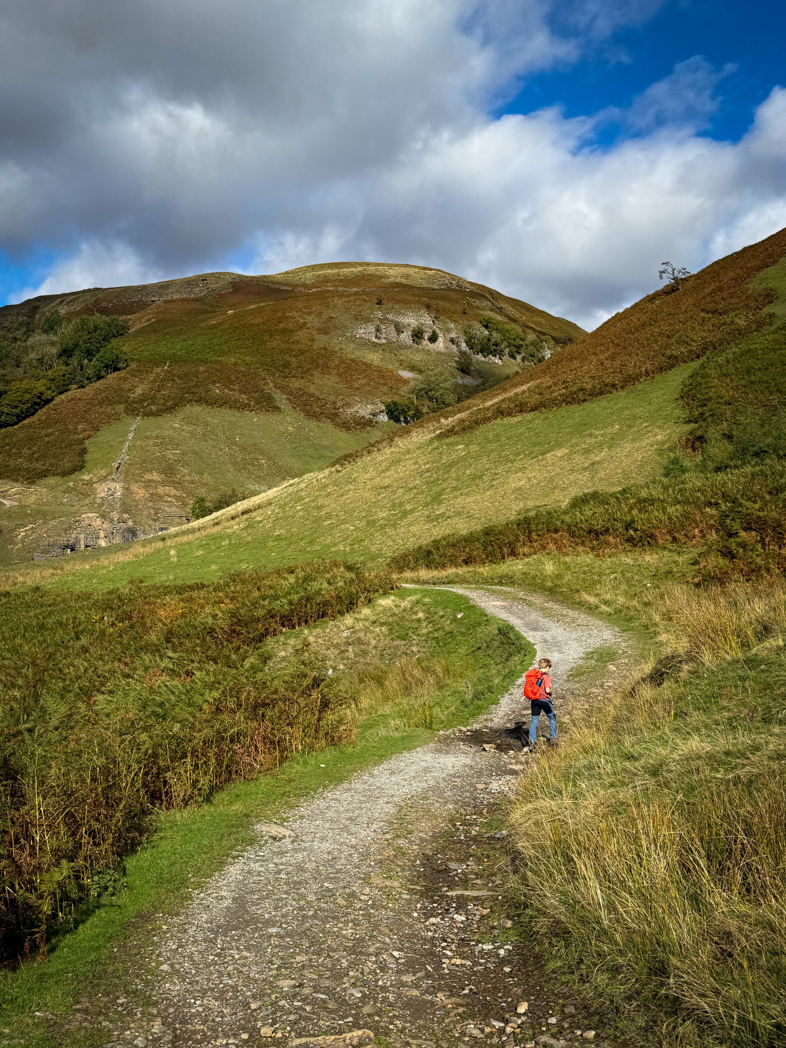 Child walking along a wide stony tracks towards a cleft in the hillside with ruins in the distance