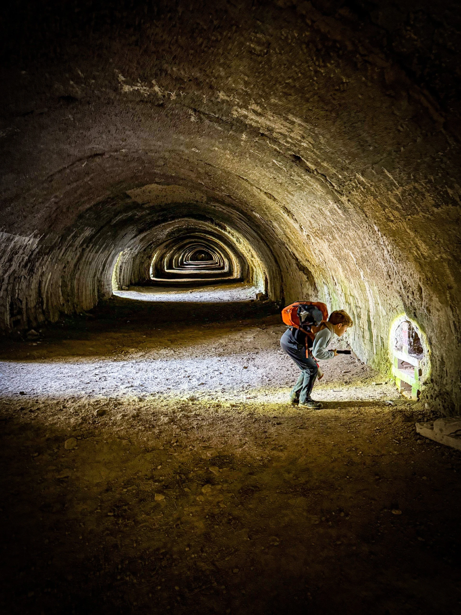 Child standing looking into a tunnel inside a huge lime kiln with light shining in from the side
