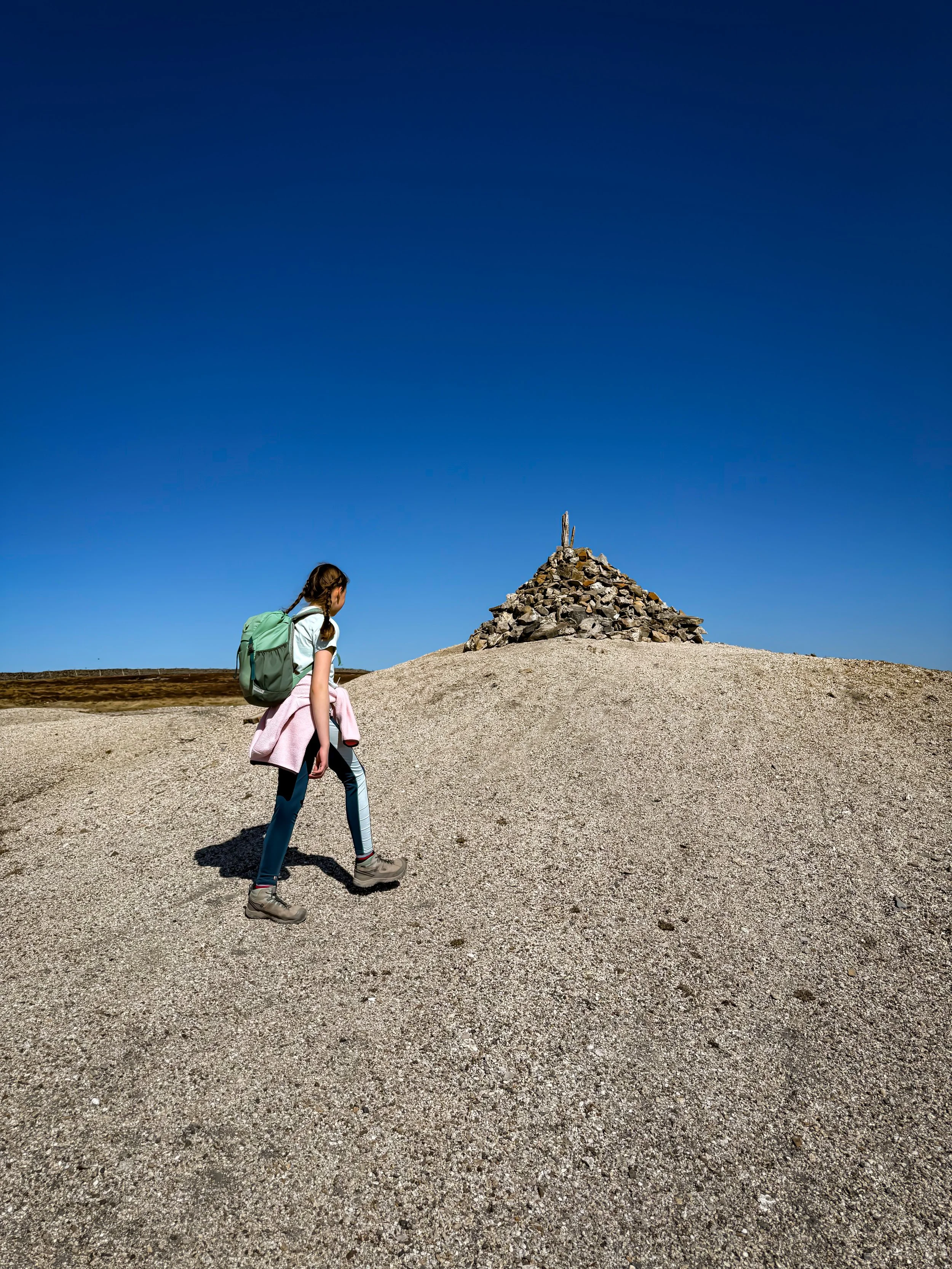 Child walking under blue skies to the summit cairn