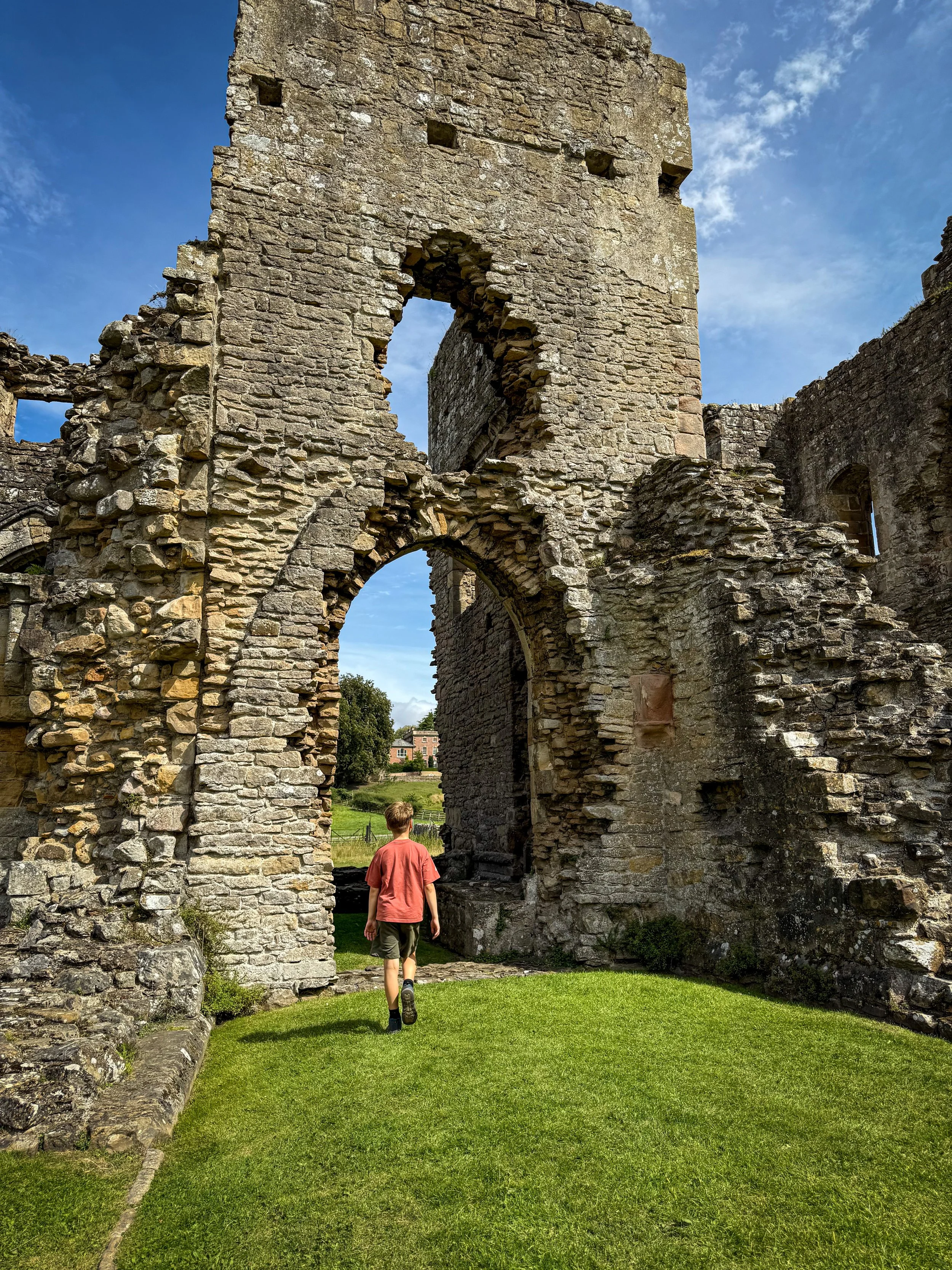 Child walking through a ruined archway under blue sky and on grass